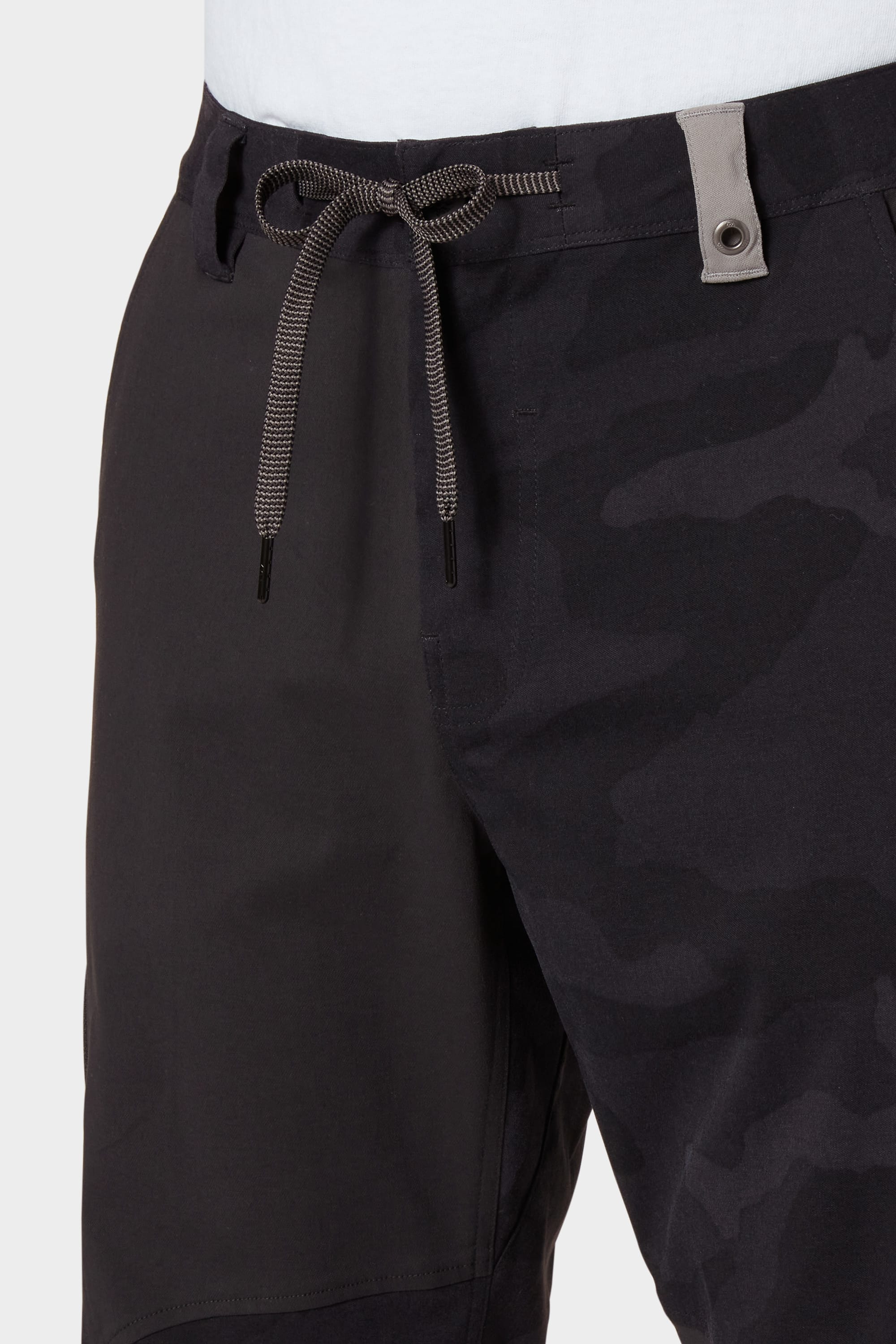 Close-up of a person in the 686 Mens Anything Cargo Pant - Relaxed Fit, featuring dark camo patterning, a grey drawstring and belt loop. These breathable pants offer 4-way stretch and a relaxed fit for all-day comfort. Brand: 686.