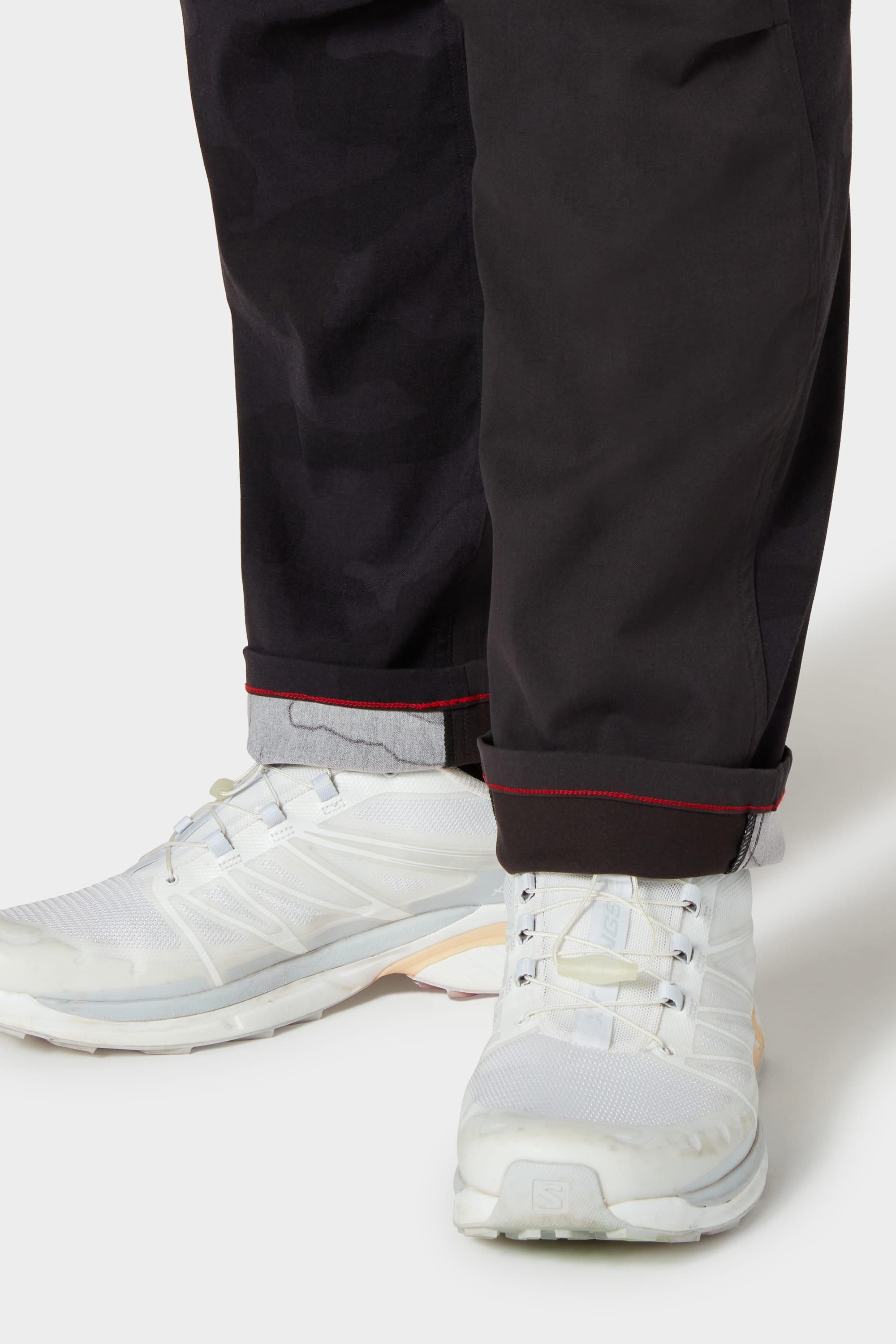 A person wearing 686 Mens Anything Cargo Pant - Relaxed Fit in black with red stitching and white sneakers stands on a white background, showcasing the breathable fabric and comfort of these 686 cargo pants.