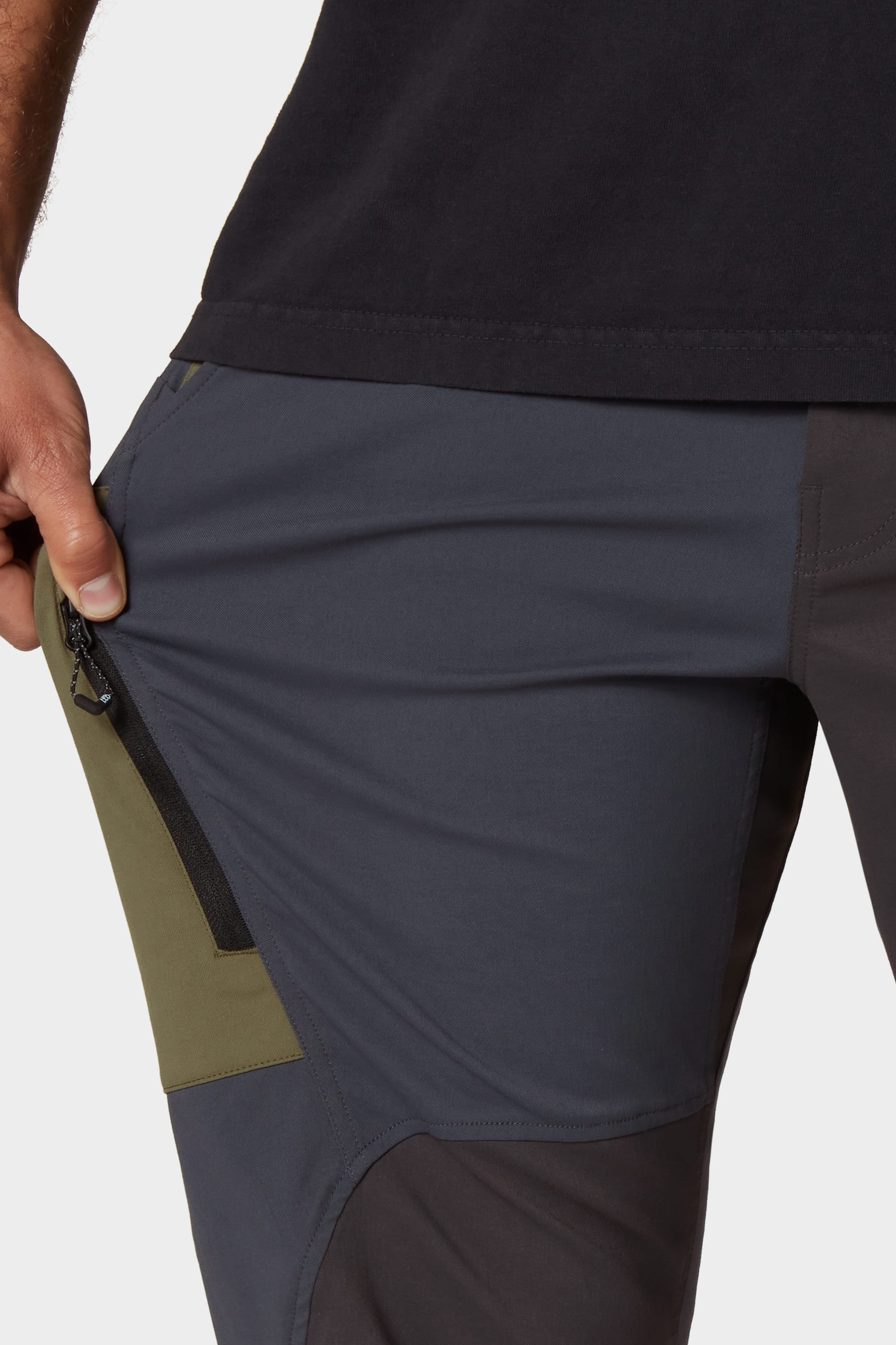 Wearing the 686 Mens Anything Cargo Pant - Relaxed Fit, someone pulls at a green side pocket zipper, showing its placement and design. The 4-way stretch fabric from 686 offers comfort with every movement.