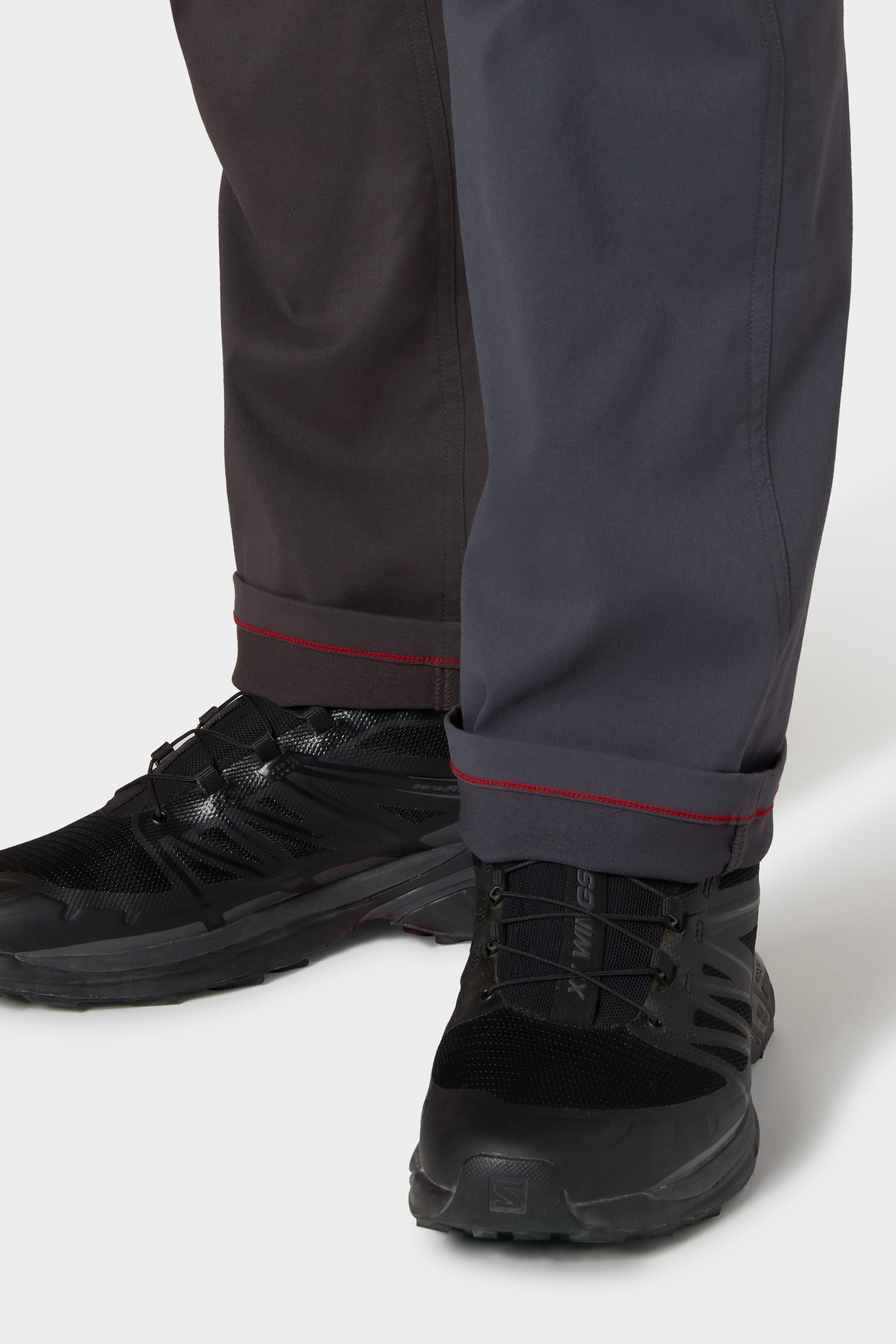 A person wears 686 Mens Anything Cargo Pant - Relaxed Fit by 686, featuring two-tone 4-way stretch fabric and red-stitched cuffs, paired with black athletic shoes on a white background.