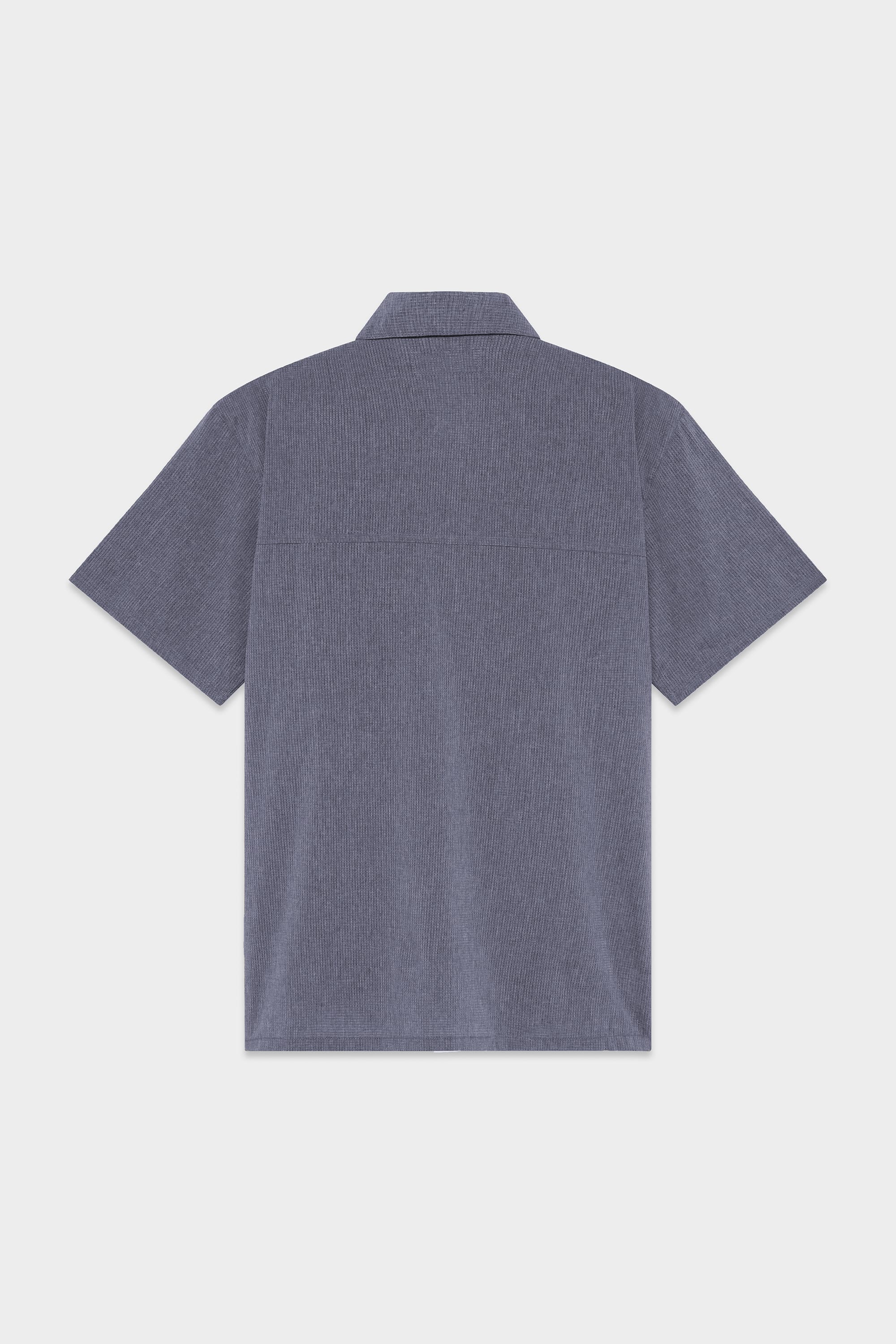 Back view of the 686 Mens Seeker Perforated Button Up by 686, featuring short sleeves, a collar, straight hem, and textured blue fabric. Displayed against a light gray background.