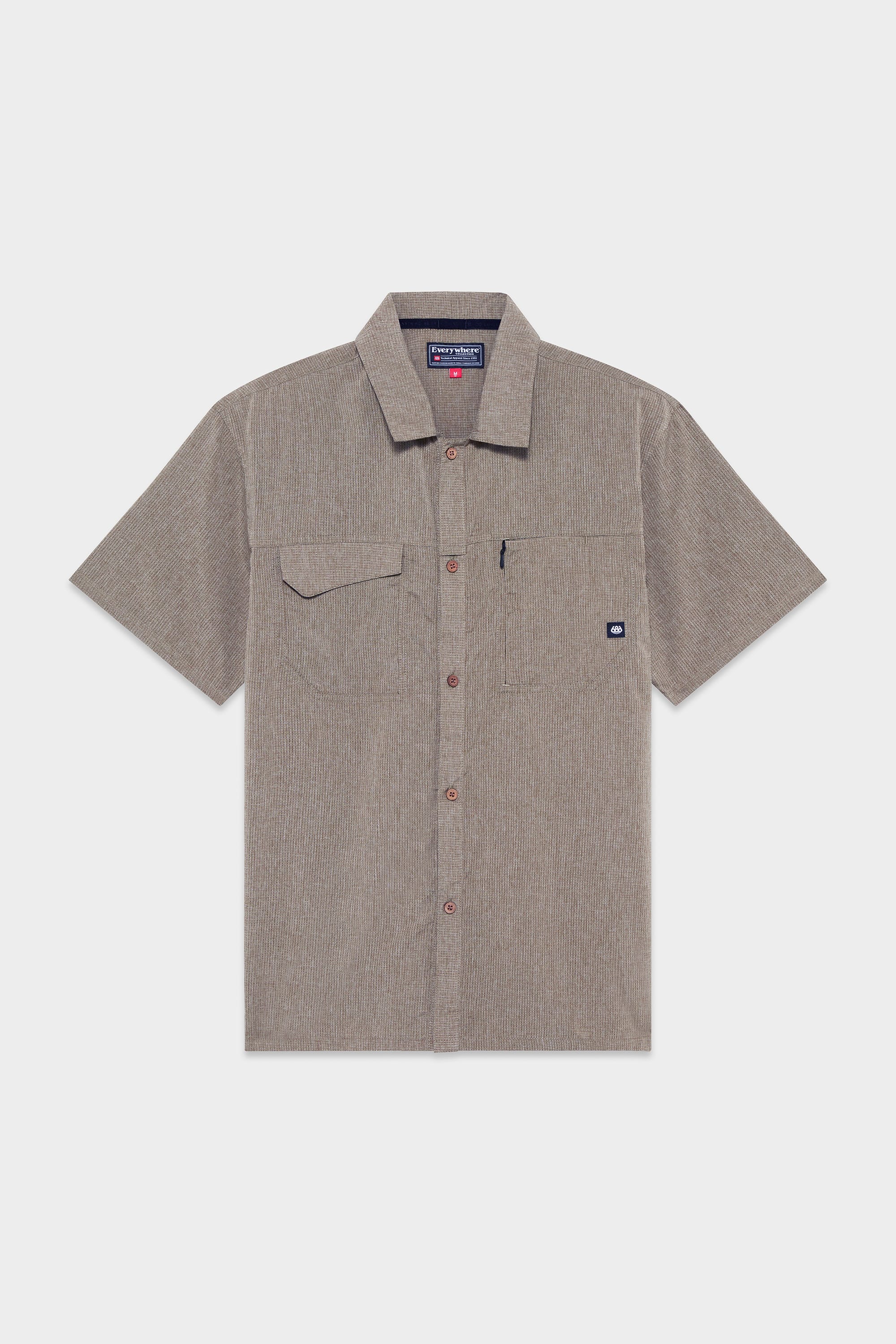 The 686 Mens Seeker Perforated Button Up is a light brown, short-sleeve shirt with subtle stripes, a left chest pocket with flap and logo tag, shown on a plain white background.