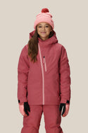 A smiling girl wears the 686 Girls' Hydra™ Insulated Jacket with body-mapped lining for warmth, matching pants, a light pink knit hat with a red pom-pom, and gloves, standing against a plain light background.