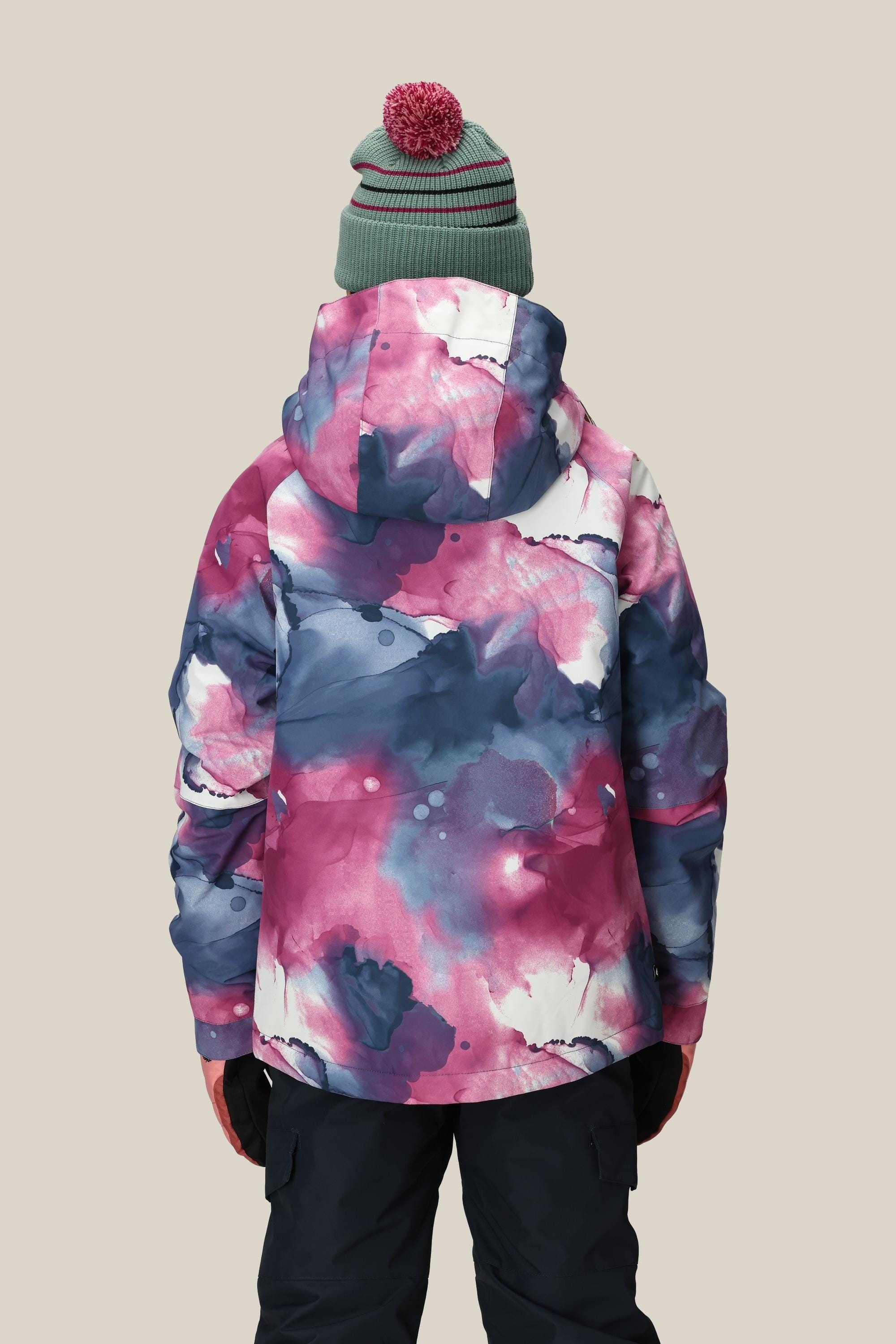 A person is seen from behind wearing the 686 Girls' Hydra™ Insulated Jacket by 686 in a blue, pink, and white watercolor pattern with body-mapped lining for warmth, paired with black pants, black gloves, and a green knit beanie with a red pom-pom.