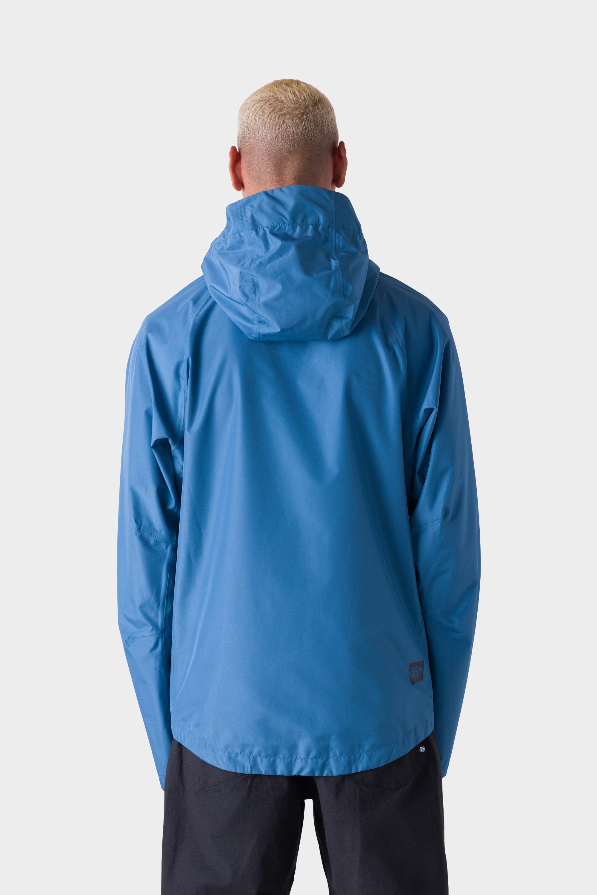 A person with short blond hair is seen from behind, wearing the 686 Men's Hydra™ 2.5L All-Weather Jacket by 686 in blue and black pants against a plain white background.