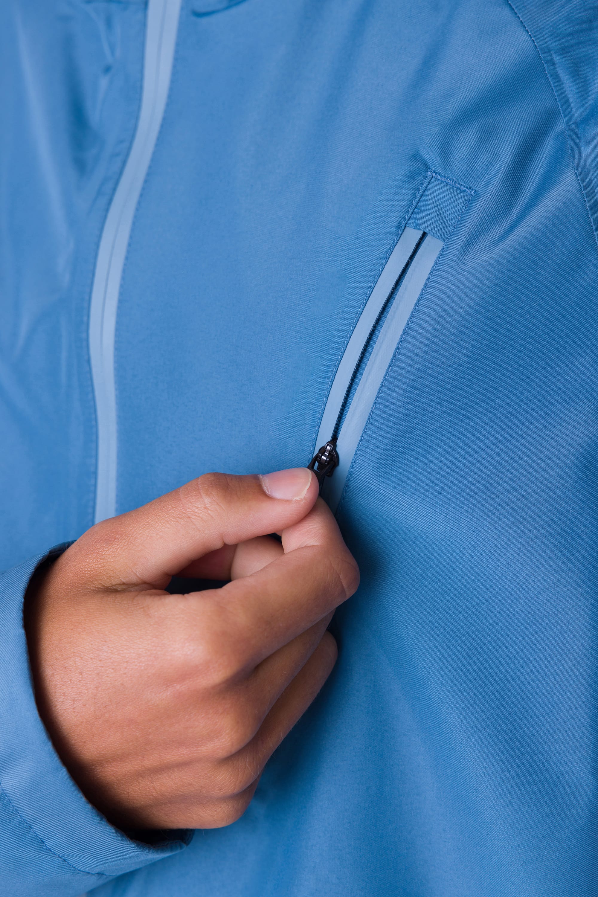 A hand unzips the vertical chest pocket of the 686 Men's Hydra™ 2.5L All-Weather Jacket, offering a close-up look at the blue fabric and zipper details from 686.