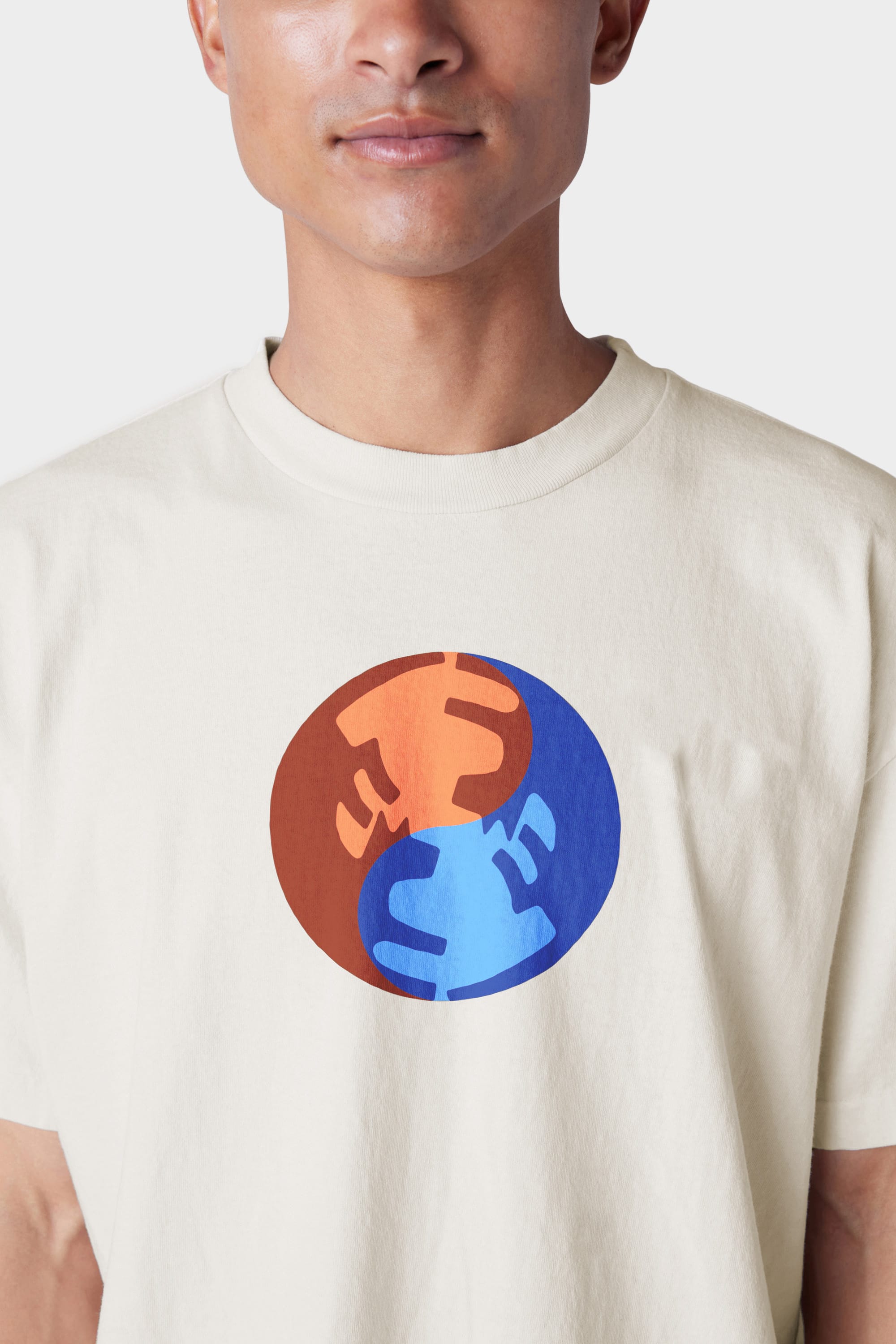 A person wearing the 686 Mens Bark and Bite Short Sleeve Tee by 686, featuring a cream color and chest graphic of two abstract faces—one orange in a red circle, one blue in a blue circle—facing each other.
