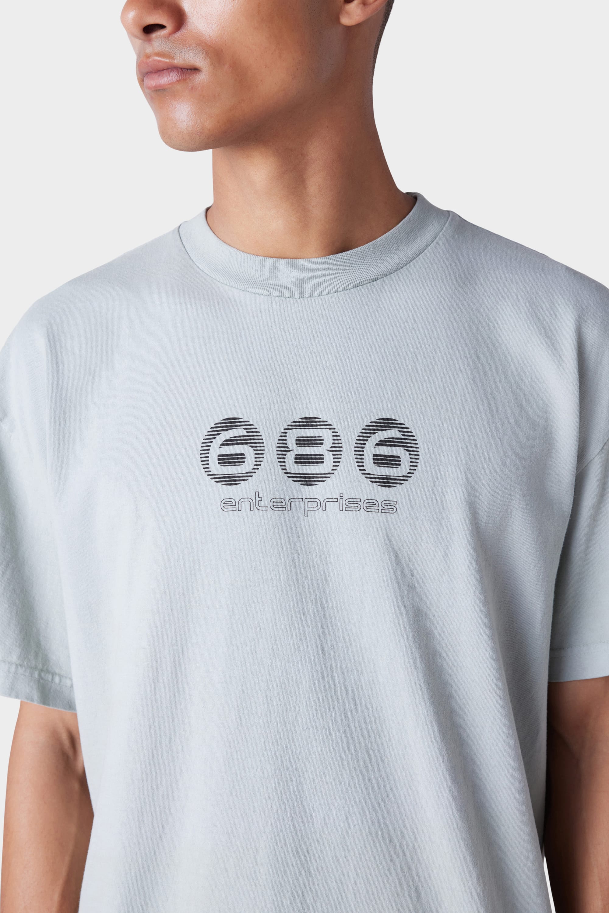 A person models the 686 Mens Blur Short Sleeve Tee, a light gray shirt featuring stylized black 686 branding on the chest, shown from shoulders to mid-torso against a plain background.