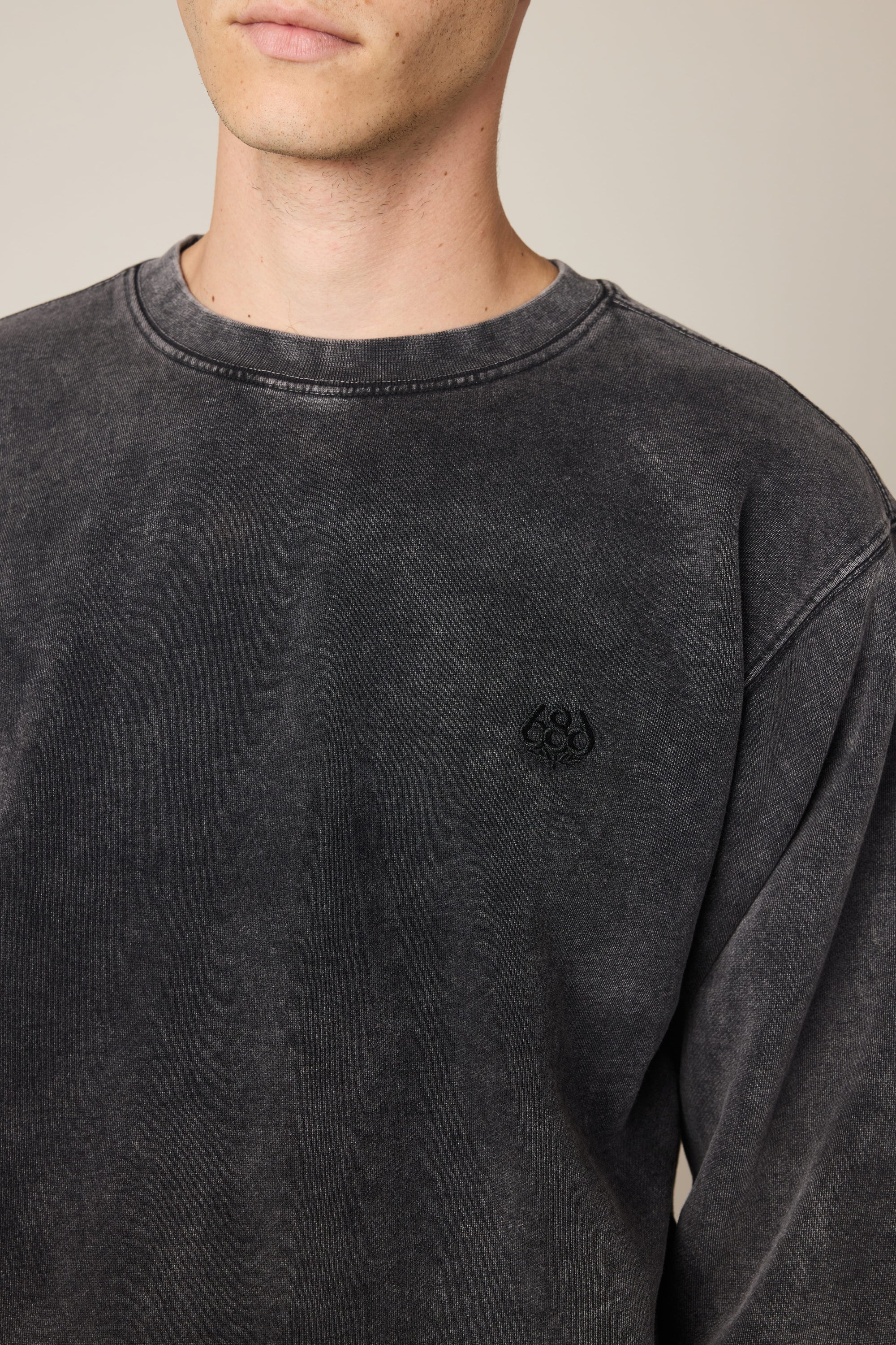 A person wears the 686 Wreath Relaxed LS Crewneck, a faded black 100% cotton sweatshirt with a small embroidered logo on the left chest, shown from shoulders to mid-torso against a plain background. Brand: 686.