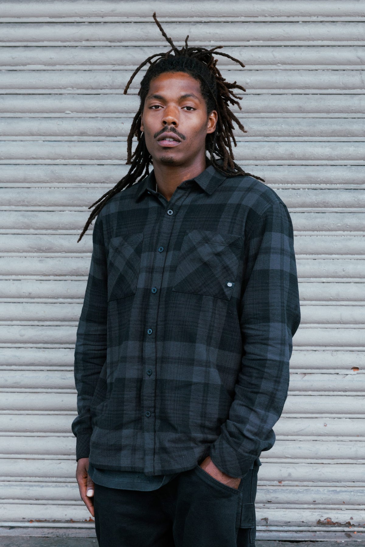A man with dreadlocks wears a black and grey 686 Men’s SMARTY® Headwall Flannel.