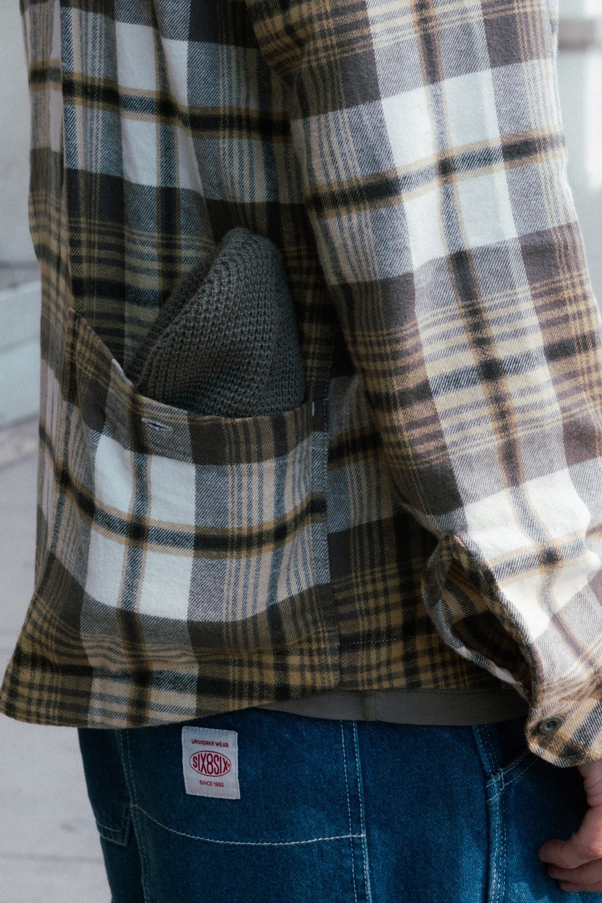 Close-up of a person wearing a brown and white 686 Men’s SMARTY® Headwall Flannel with a knit beanie tucked into the chest pocket.