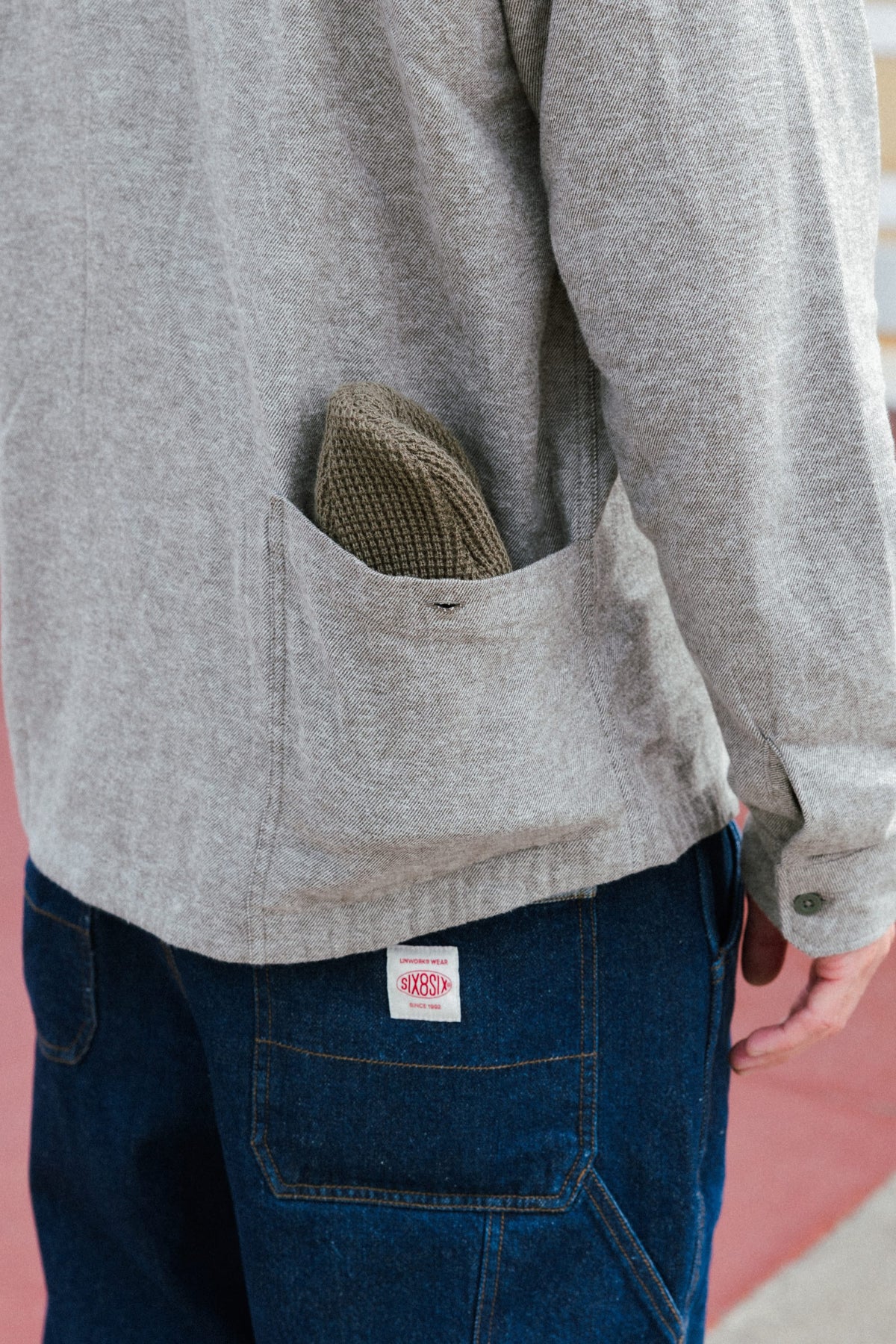 A light gray 686 Men’s SMARTY® Headwall Flannel with a pocket on the back containing a small knit cap, worn over dark blue denim pants.