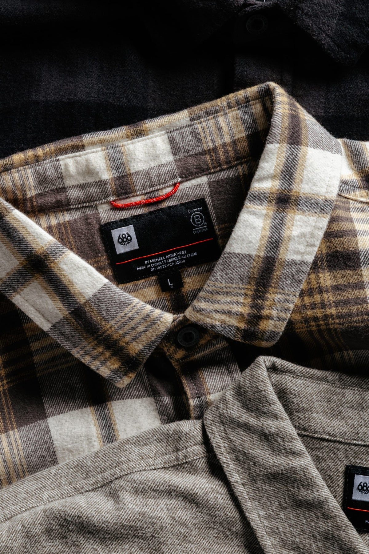 Close-up of stacked 686 Men’s SMARTY® Headwall Flannel shirts, showing the collars, buttons, and interior clothing labels.