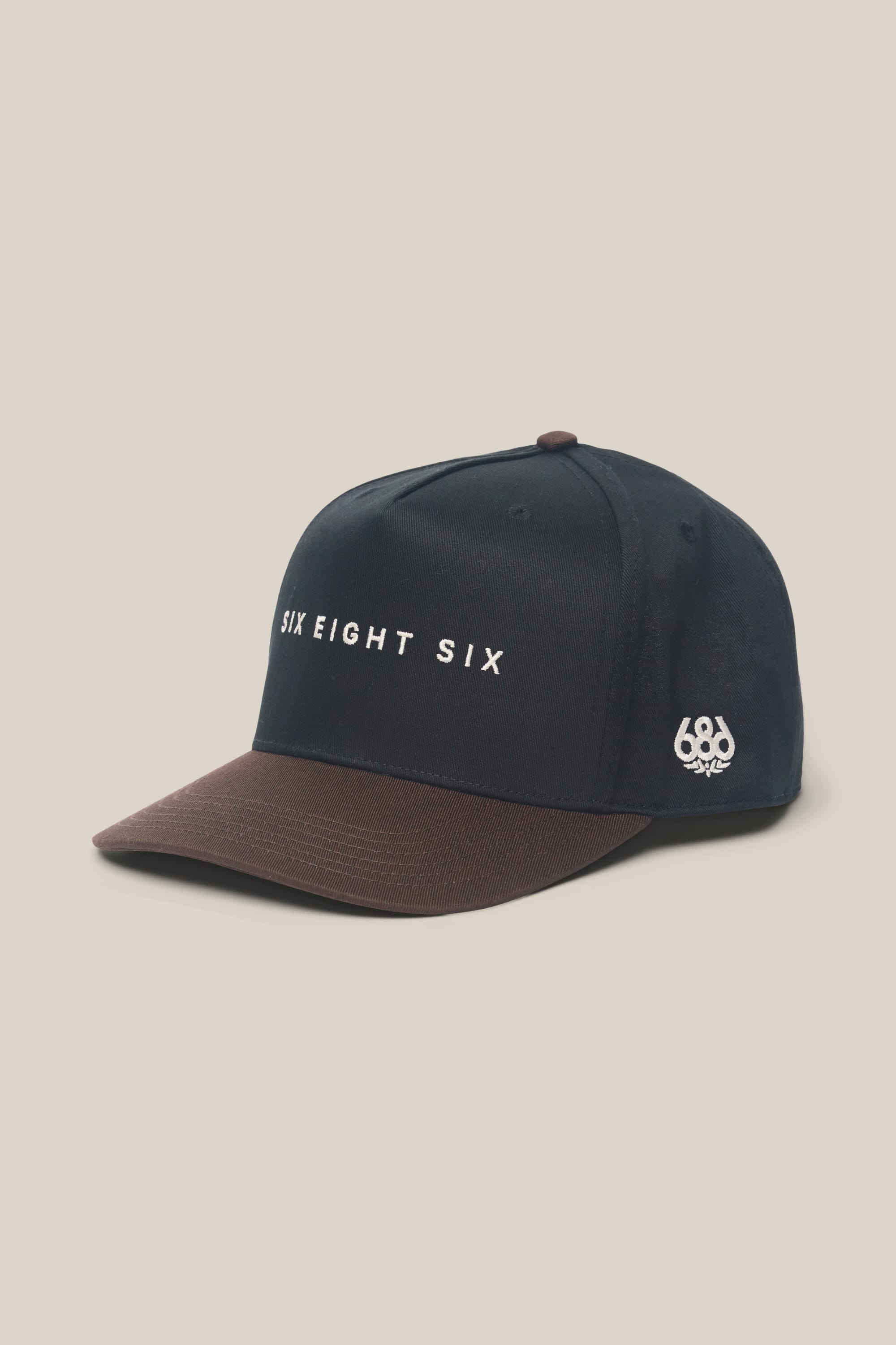 The 686 High-Pro Ses Two Tone Structured 5 Panel Hat is a black cotton men's cap with a brown brim, featuring "SIX EIGHT SIX" embroidered in white on the front and a small 686 logo on the side. Made from 100% cotton.