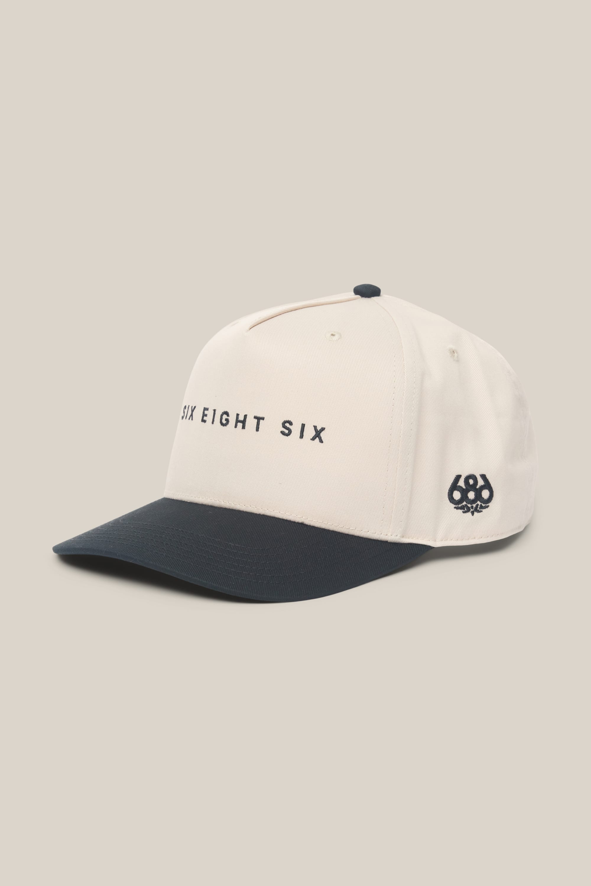 The 686 High-Pro Ses Two Tone Structured 5 Panel Hat by 686 is a white cotton men's hat with a black brim, SIX EIGHT SIX text on the front, and a small 686 logo on the side, shown on a beige background.