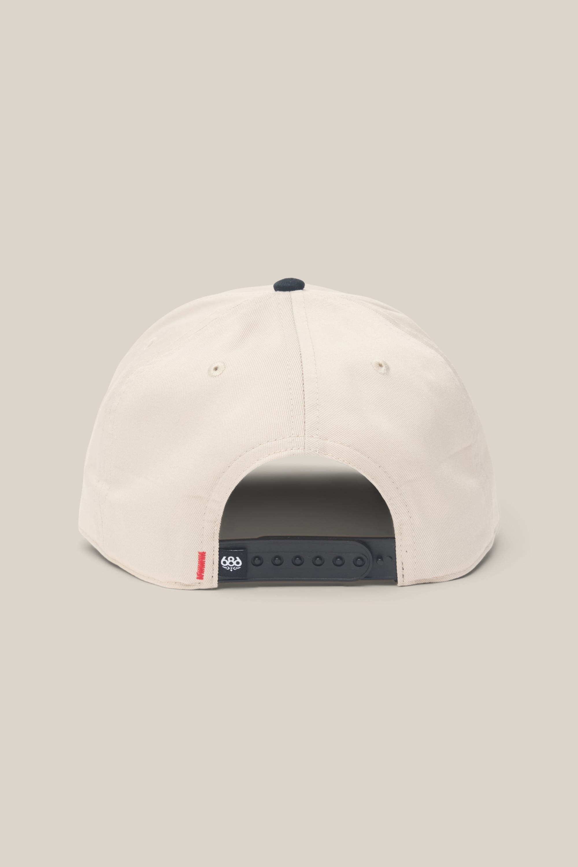 The 686 High-Pro Ses Two Tone Structured 5 Panel Hat by 686 is a beige men’s hat shown from the back, with a black adjustable snapback strap and a small red tag on the left above the strap, made from 100% cotton, set against a neutral background.