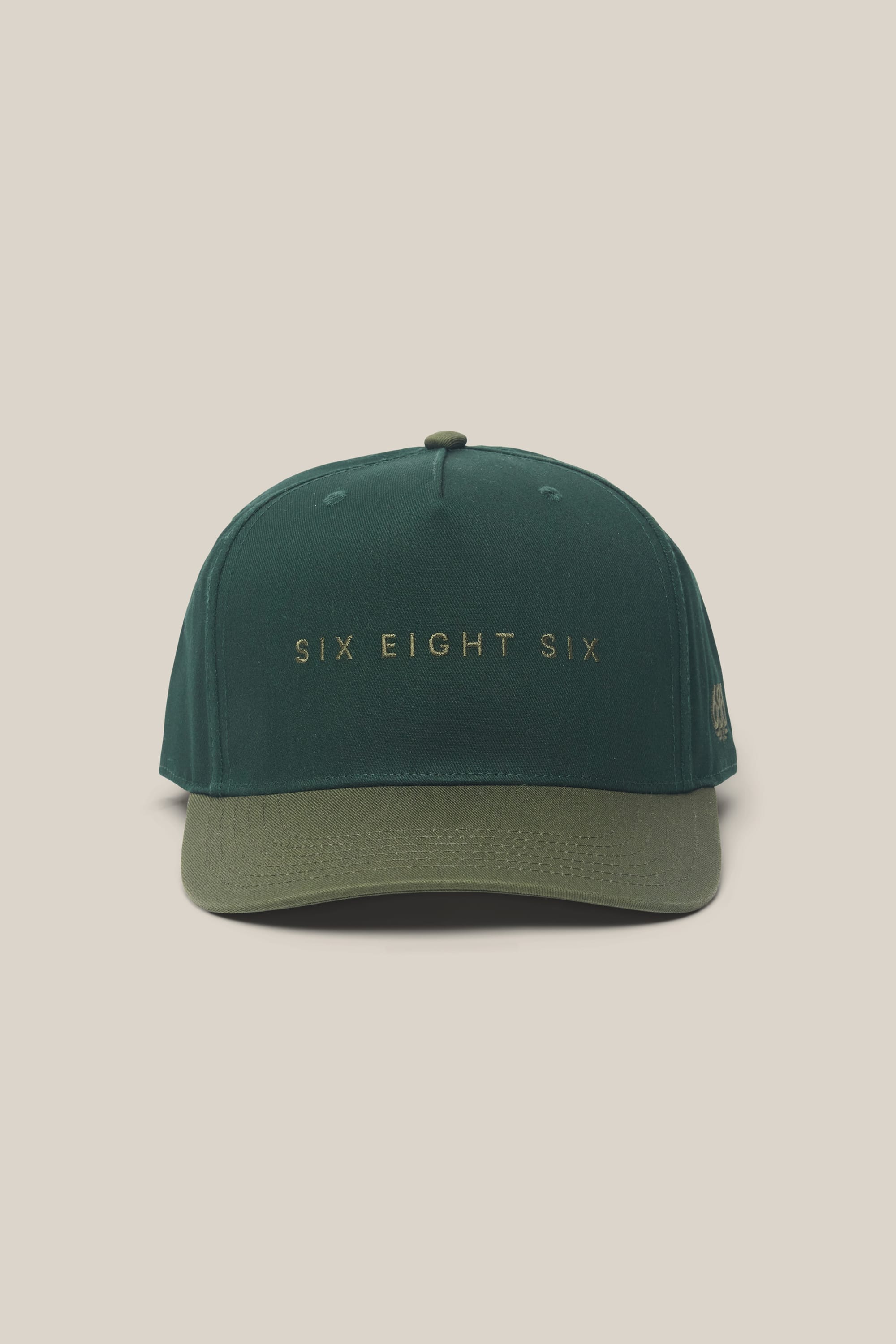 The 686 High-Pro Ses Two Tone Structured 5 Panel Hat by 686 features "SIX EIGHT SIX" embroidered in gold lettering on the front of its green cotton fabric, and is showcased against a plain beige background.