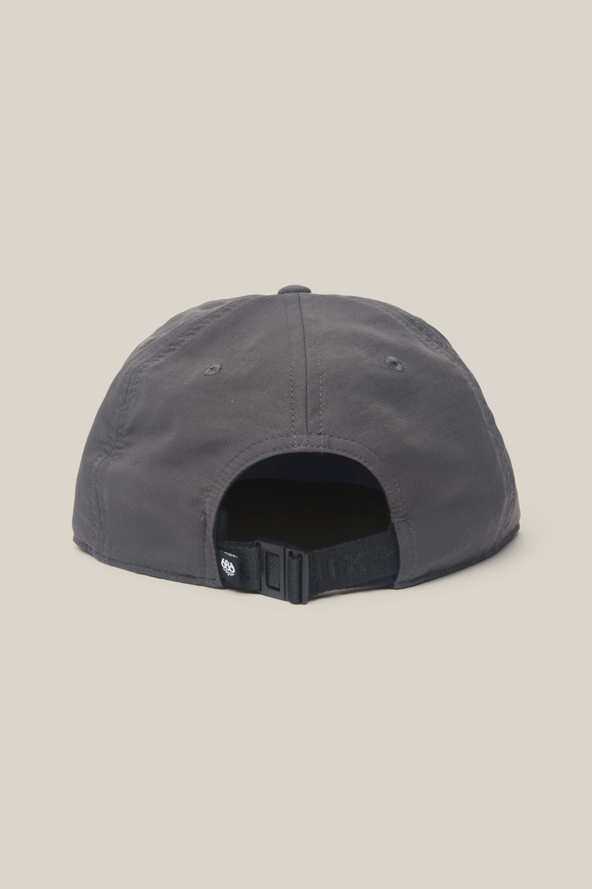 The 686 Low-Pro Adventure Unstructured 6 Panel Hat by 686 is a dark gray men’s polyester cap, shown from the back with an adjustable strap, black buckle, and small black tag, set against a plain beige background.
