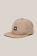 The 686 Low-Pro Adventure Unstructured 6 Panel Hat is a beige men’s poly-cotton cap with a curved brim, visible stitching, and a black front patch featuring the white 686 logo, shown on a light beige background.