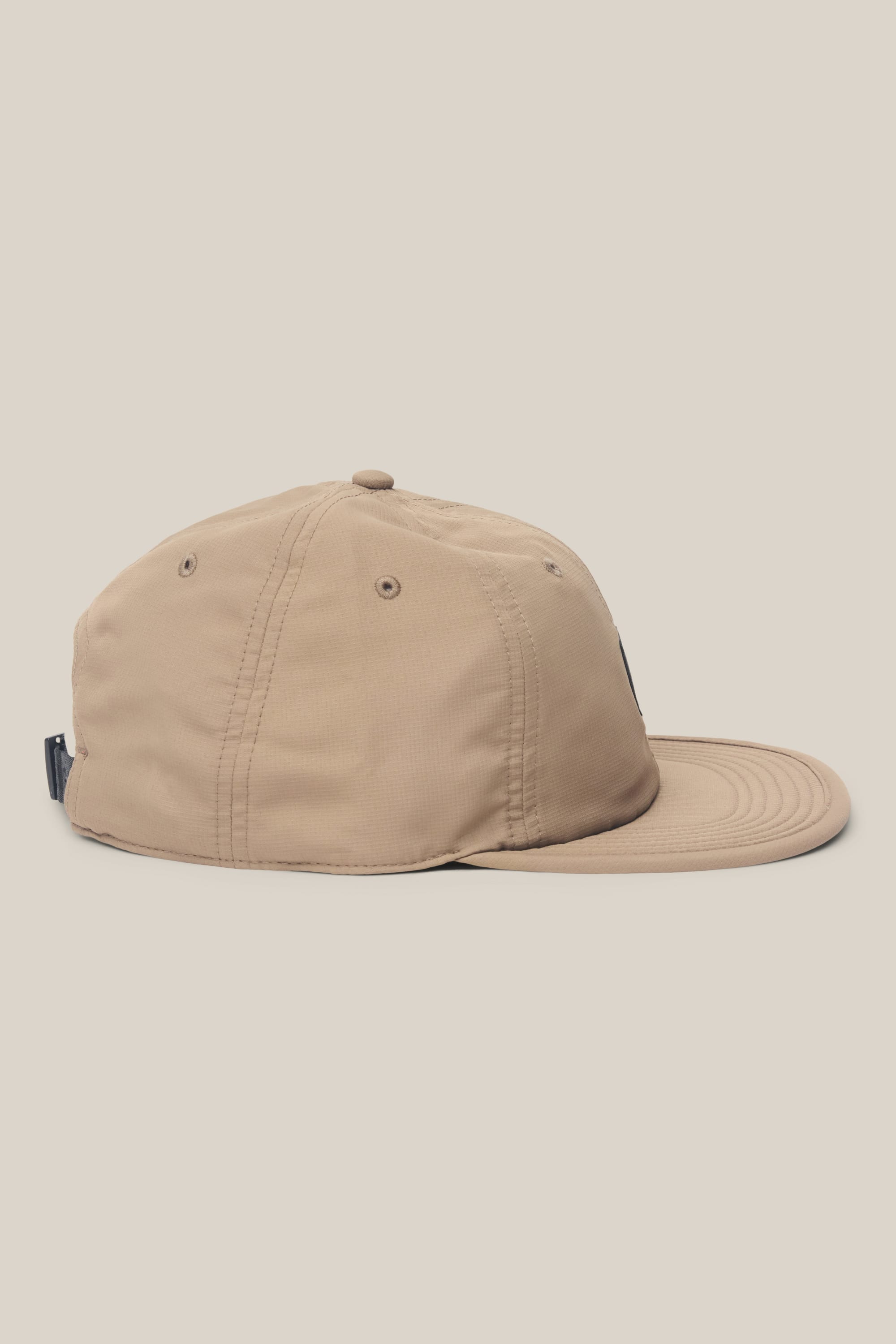The 686 Low-Pro Adventure Unstructured 6 Panel Hat by 686 is displayed in beige polyester cotton from the side, showcasing visible stitching, crown eyelets, and a slightly curved brim against a plain light background.