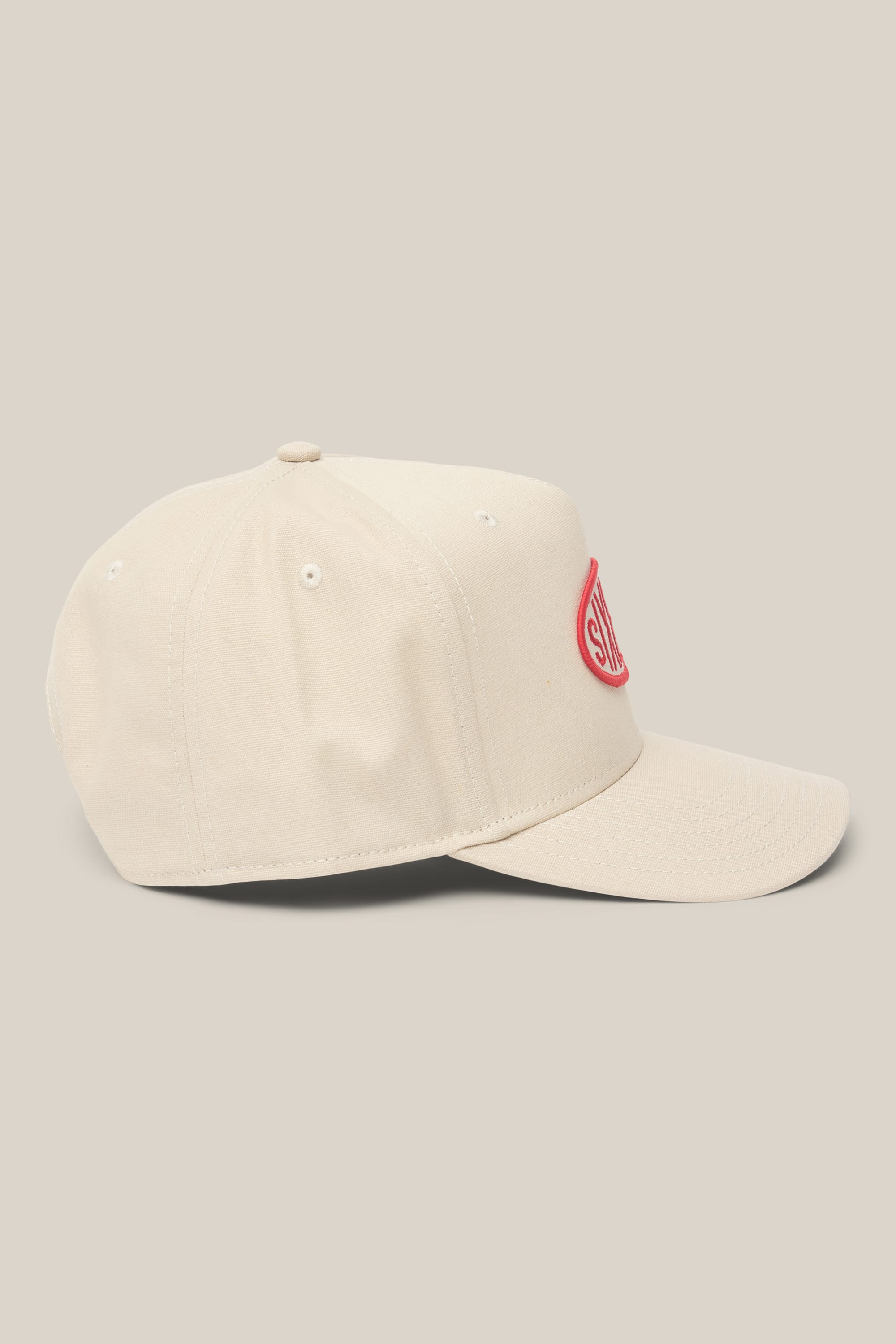 The 686 High-Pro 92 Structured 5 Panel Hat by 686 is a beige men's polyester-cotton cap with a curved brim, shown in side view. A red oval embroidered patch with white text appears on the front. The background is beige.