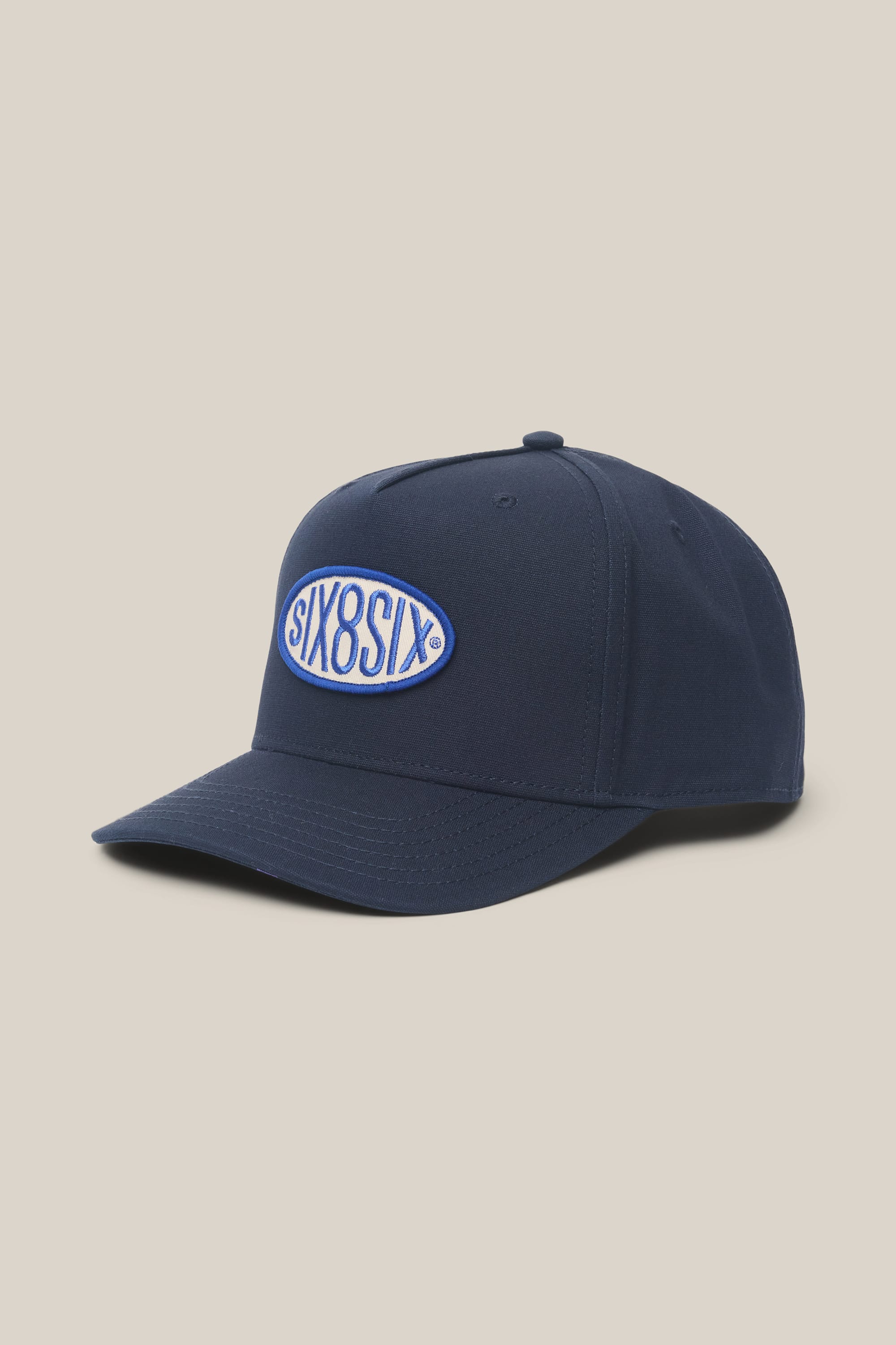 The 686 High-Pro 92 Structured 5 Panel Hat by 686 is a navy men's polyester-cotton cap with an oval front patch embroidered with SIX8SIX in white and blue, featuring a curved brim and top button, shown on a light beige background.