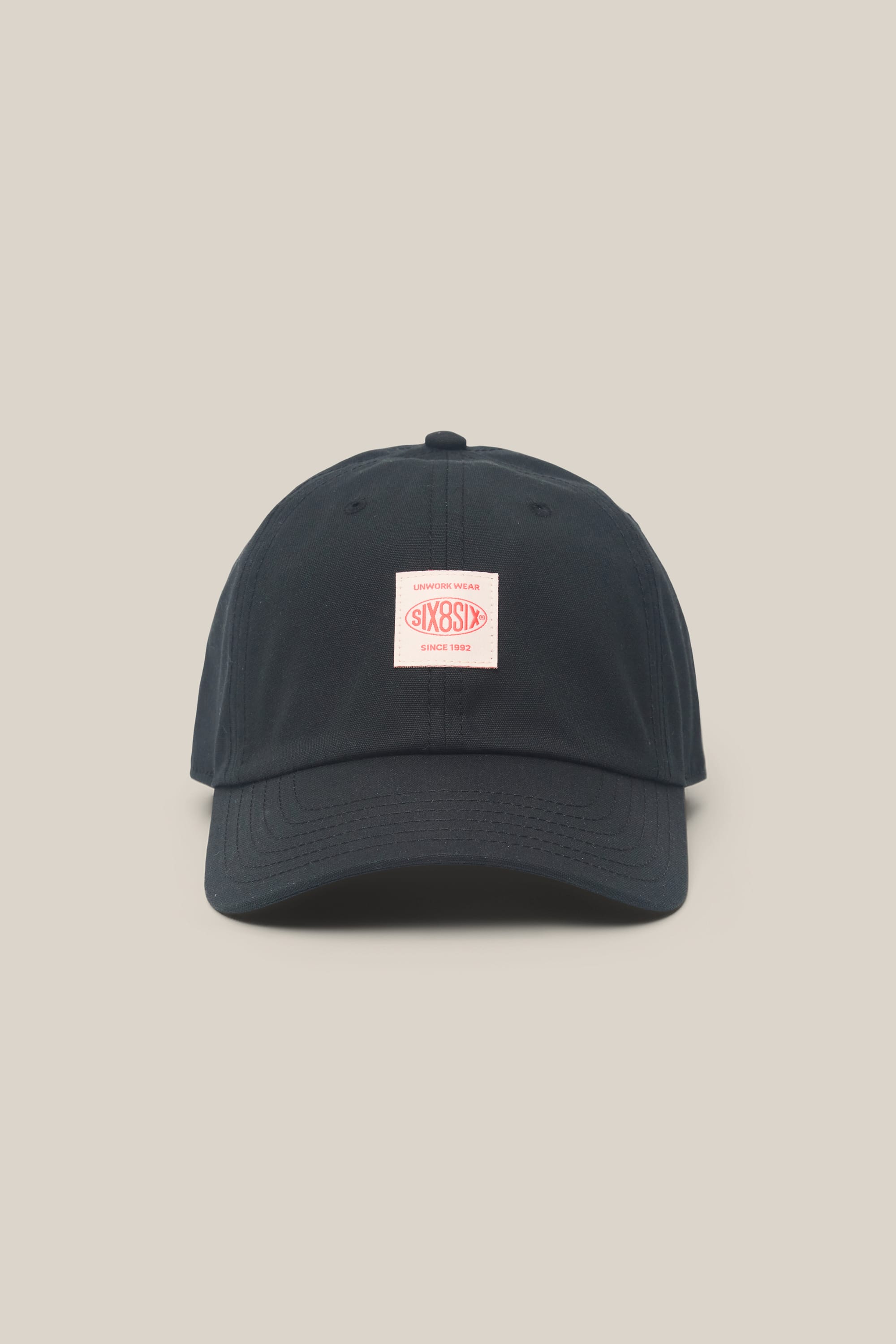 A 686 Low-Pro Unwork Unstructured 6 Panel Hat in black polyester cotton, featuring a curved brim and a small pink and white rectangular patch with text on the front. This men's woven hat by 686 is photographed against a plain beige background.