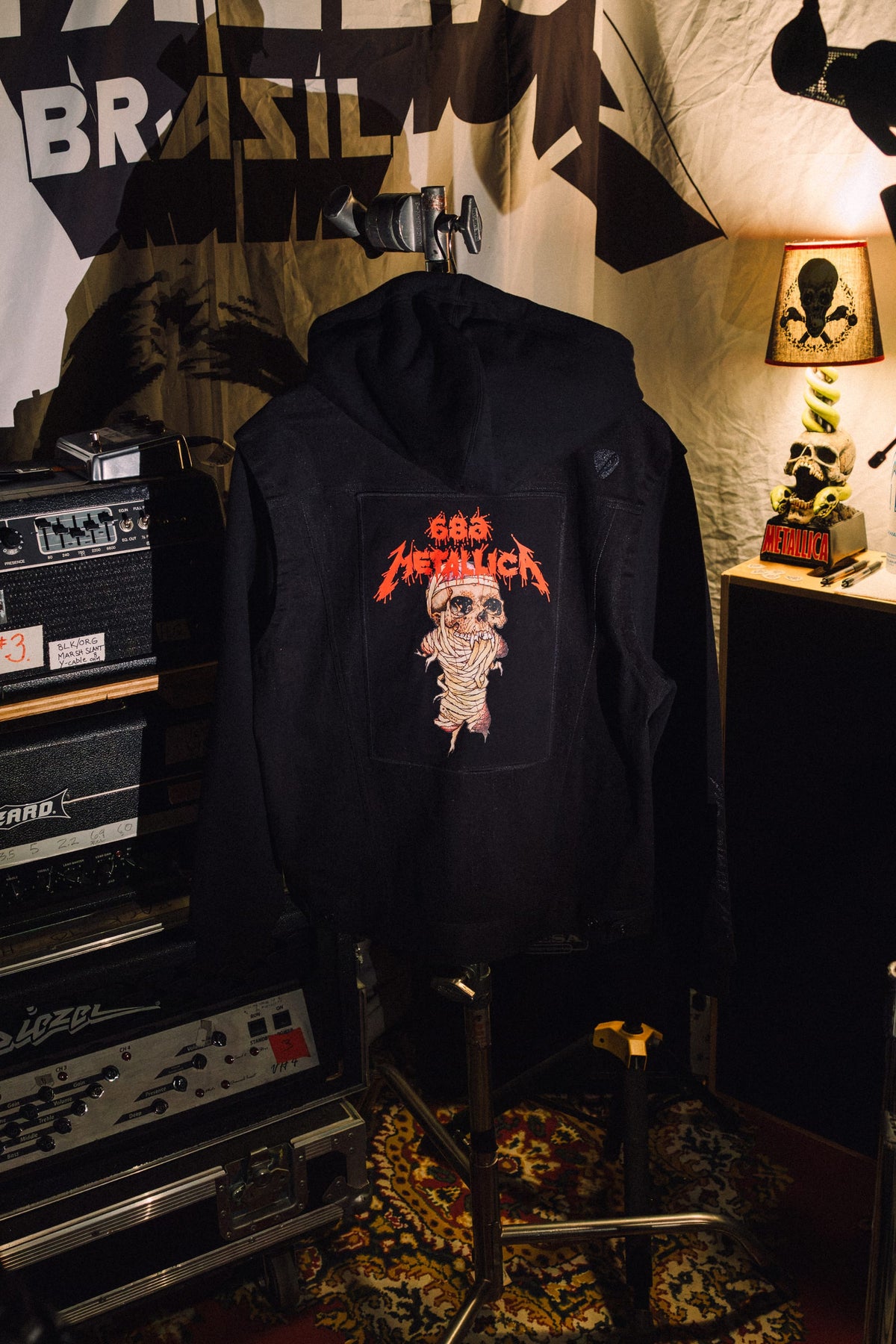 Black 686 Men’s Metalhead Trucker Jacket in denim, featuring a hood and a rectangular back patch with a skull wrapped in bandages and orange Metallica-style text.