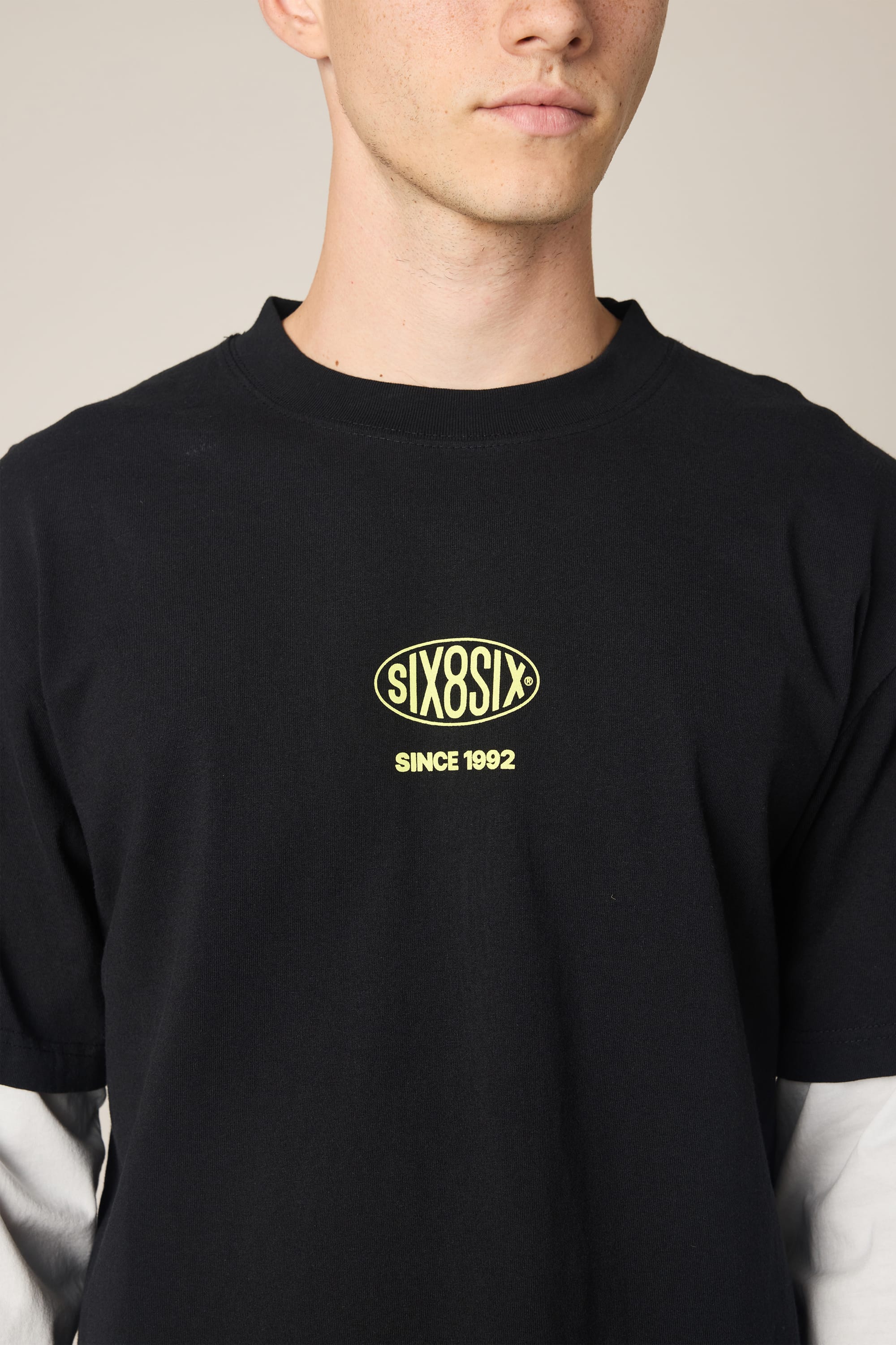 A person wearing the 686 Men's 92 Relaxed LS Double Trouble Tee, a black long-sleeve featuring a yellow 686 logo and "SINCE 1992" text. The cropped image highlights its soft, 100% cotton fabric against a plain background.