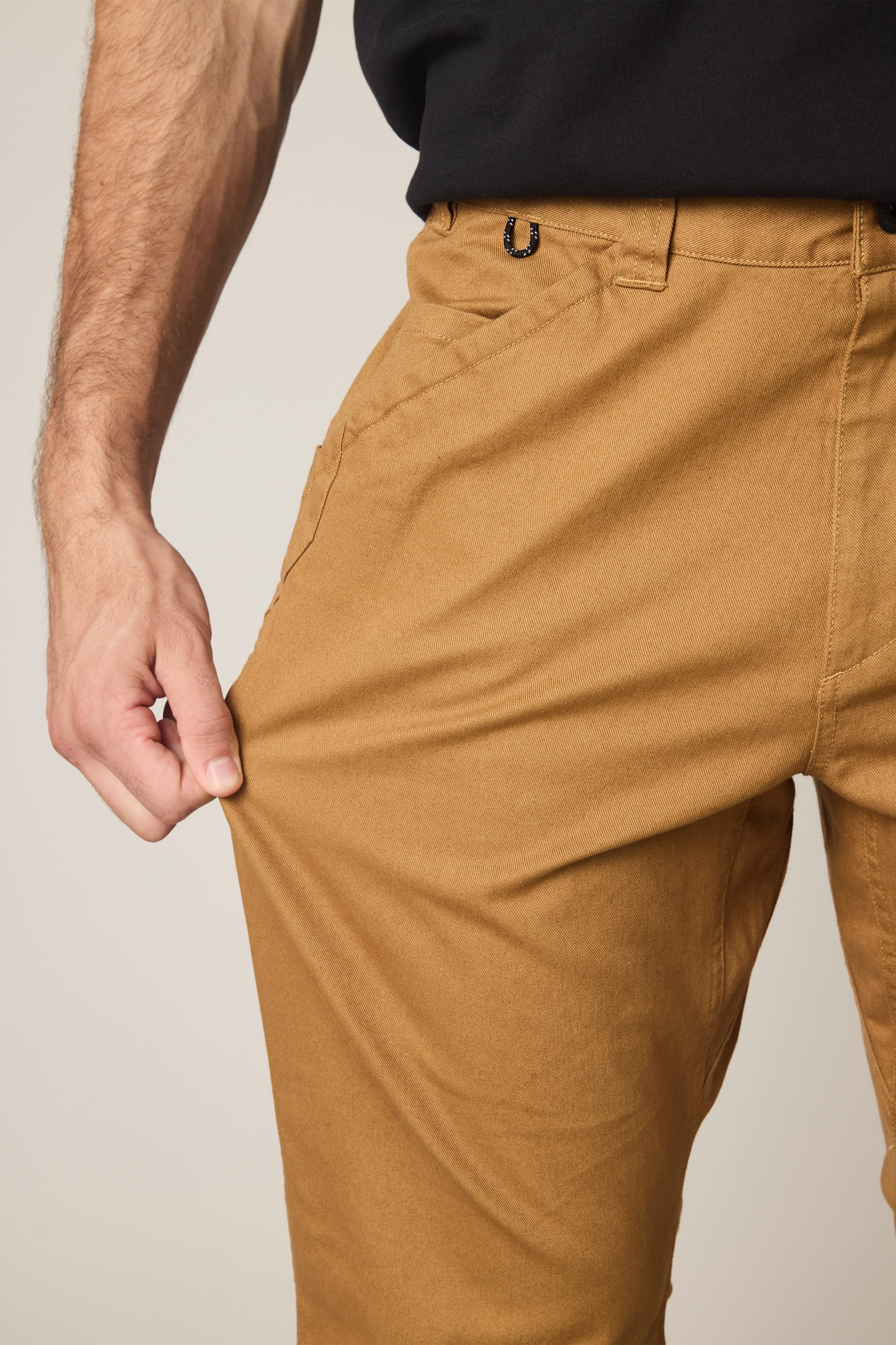 A person in 686 Men's Unwork® Tradesman Pant - Relaxed Fit by 686 and a black shirt pinches the thigh fabric, demonstrating its impressive stretch.