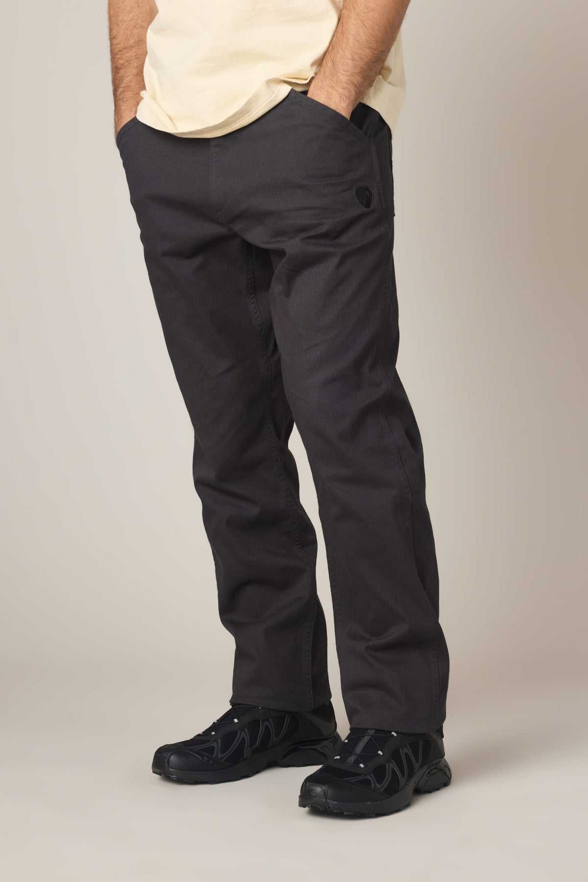 A person wearing 686 Men’s Unwork® Tradesman Pant - Relaxed Fit in charcoal grey with side pockets and black athletic sneakers.
