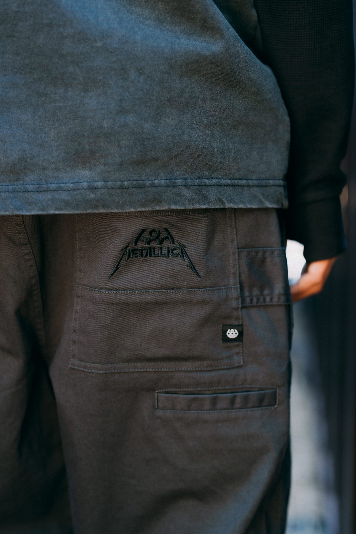 Close-up of the back pocket of 686 Men’s Unwork® Tradesman Pant in dark grey spandex, featuring an embroidered Metallica logo.
