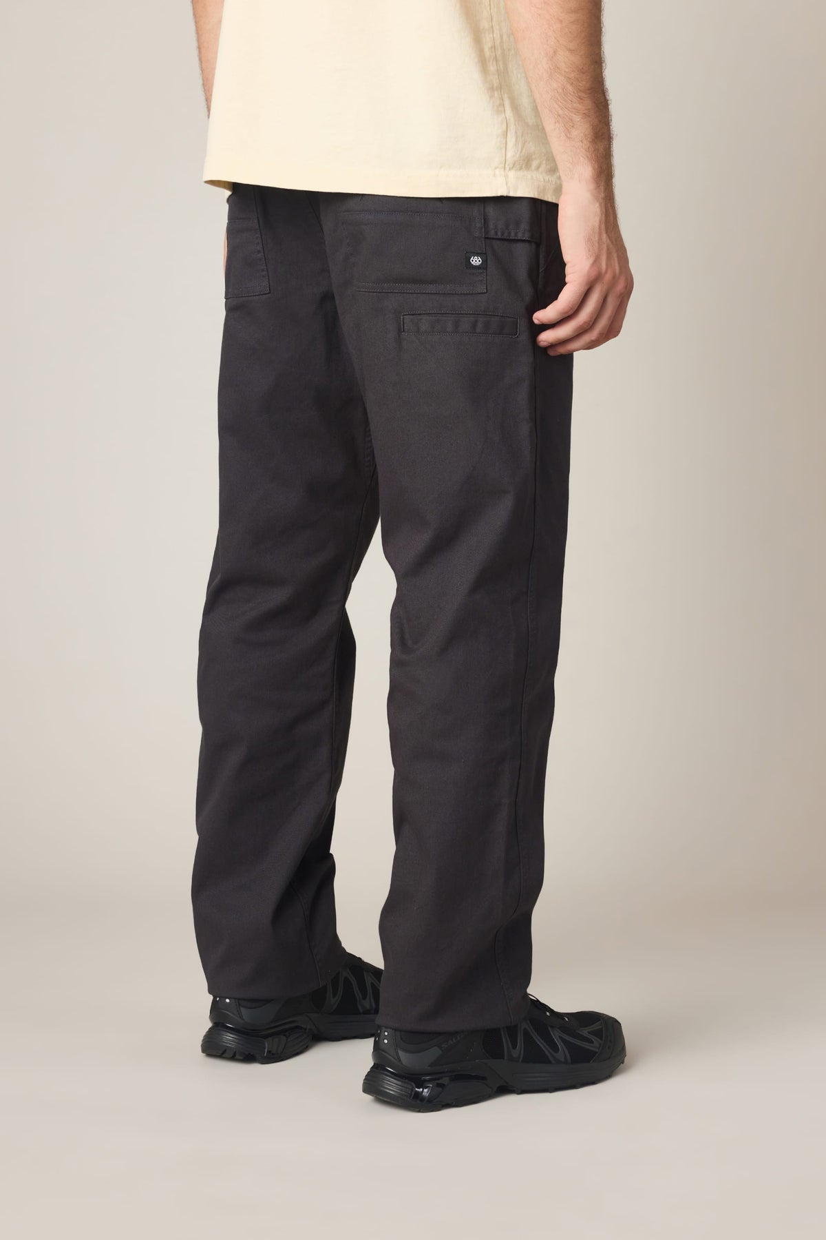 Rear view of a person wearing black relaxed-fit 686 Men’s Unwork® Tradesman Pant - Relaxed Fit nylon woven pants and black athletic sneakers.