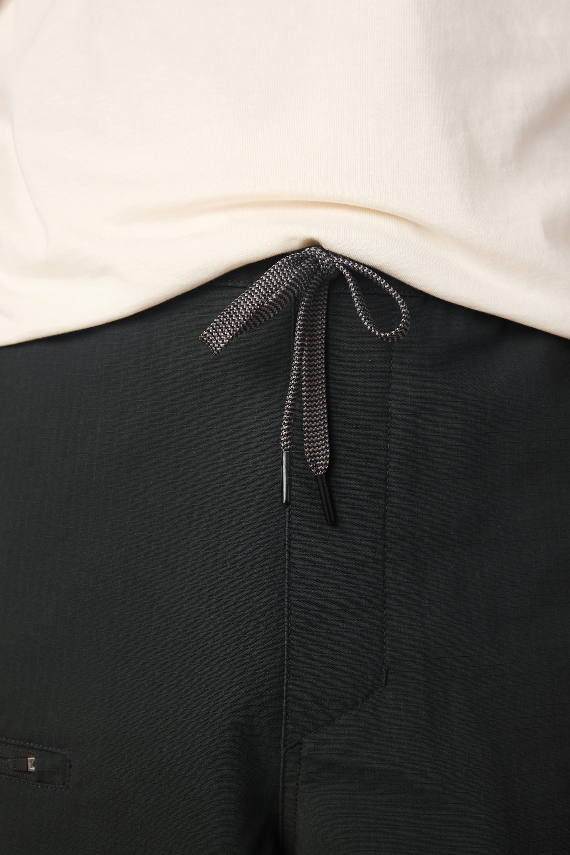 Close-up of a person wearing the 686 Men's Free Loader Pant - Loose Fit by 686, featuring a cream shirt, a black-and-white drawstring tied at the waist, and visible front pocket for added style.