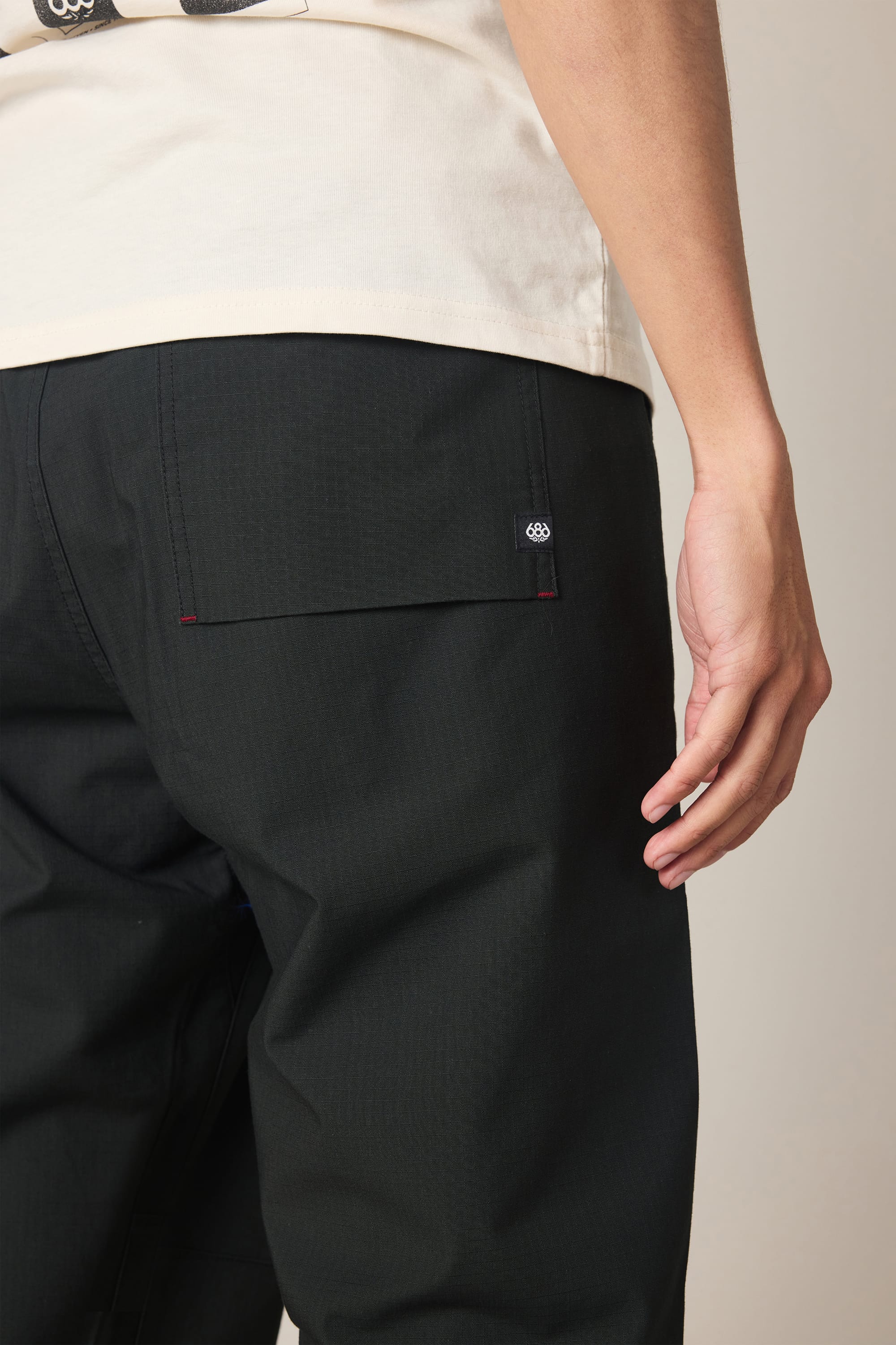 A person is shown from the side and back, one hand relaxed by their thigh, highlighting the sleek pocket design of the 686 Men's Free Loader Pant - Loose Fit by 686. The image emphasizes the modern style and details of these spandex woven pants.