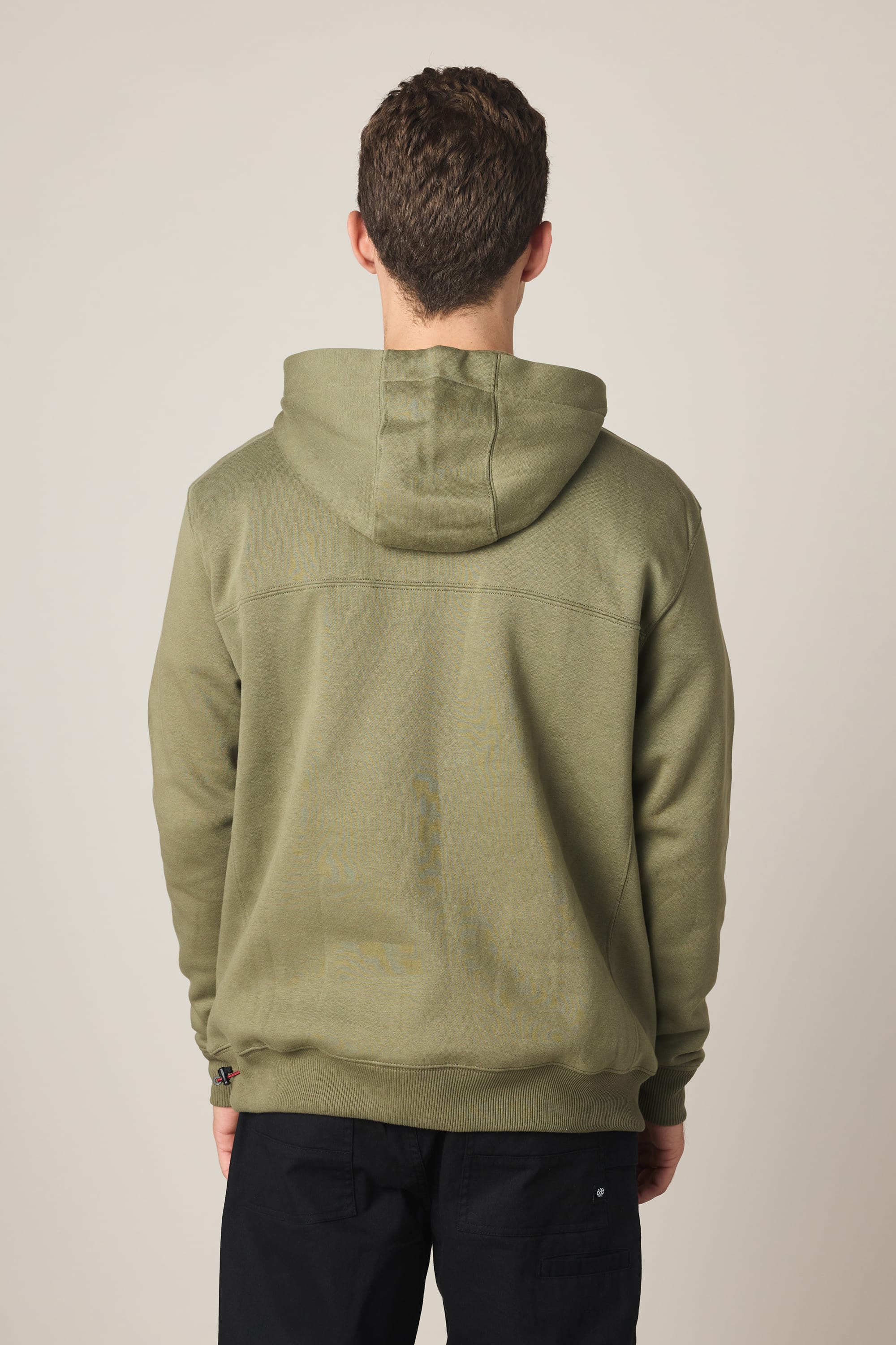 A person with short brown hair stands with their back to the camera, wearing a 686 Men's All Season Hoody in olive green and black pants against a plain light background.