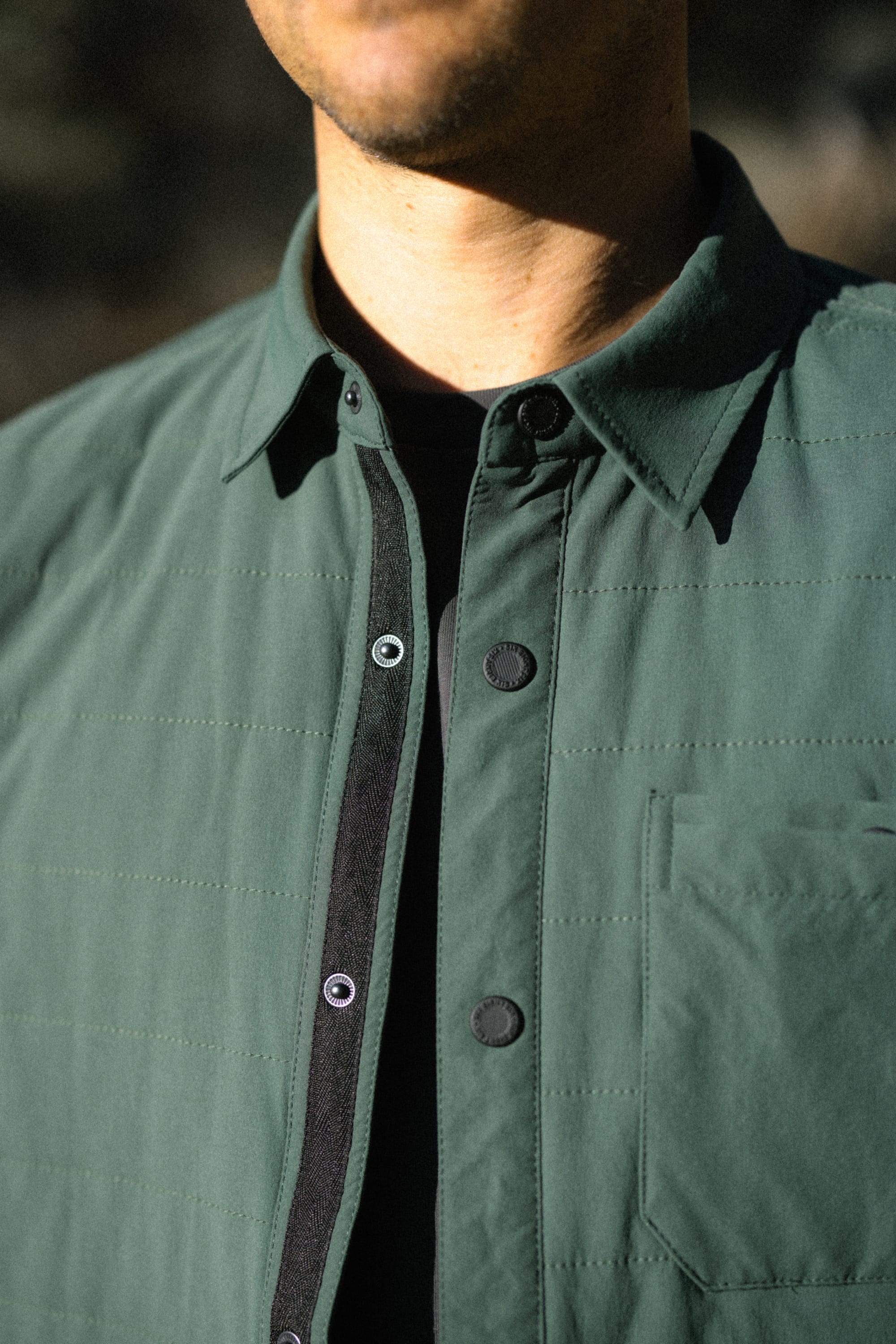A person wearing the 686 Men's Thermaldry™ Insulated Shacket in dark green over a black top, shown from the shoulders to mid-chest; the face is partially visible.