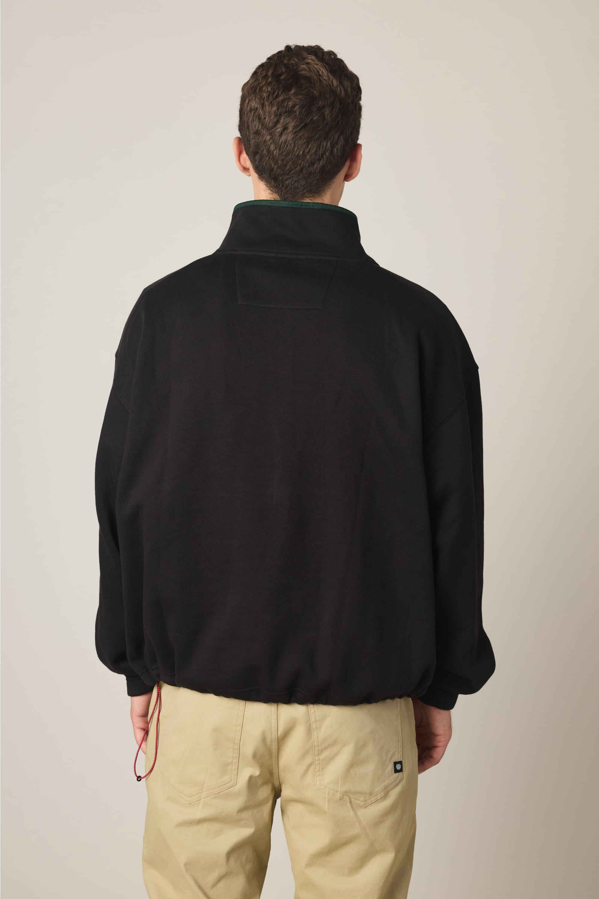 A person with short brown hair is seen from behind, wearing the 686 Men's Burnout Anorak and light beige pants, standing against a plain light background.