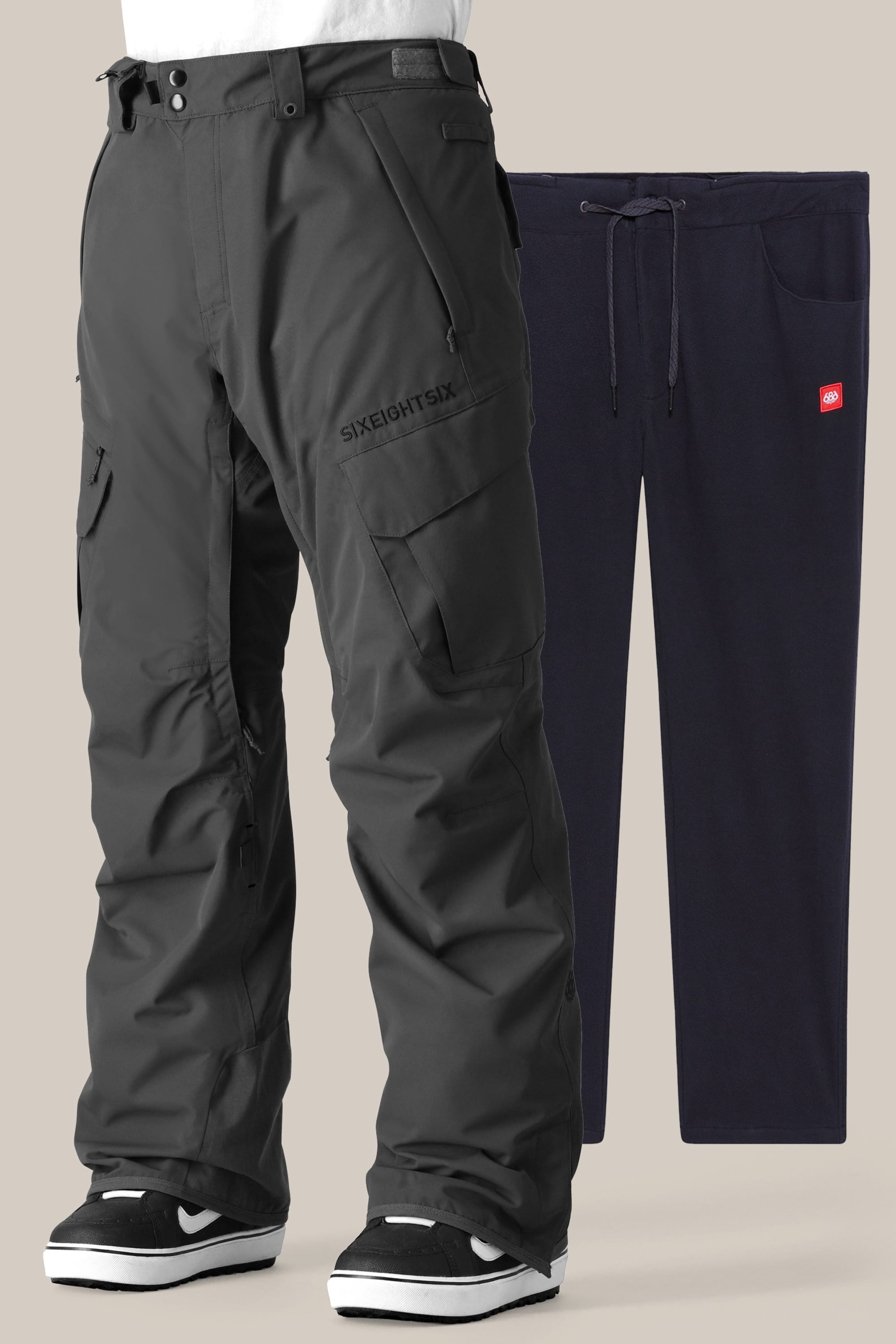 The 686 Men's SMARTY® 3-in-1 Cargo Pant in black, featuring zippered pockets, reinforced knees, and a removable sweatpant liner, is displayed in front of navy blue drawstring sweatpants with side pockets against a plain background.