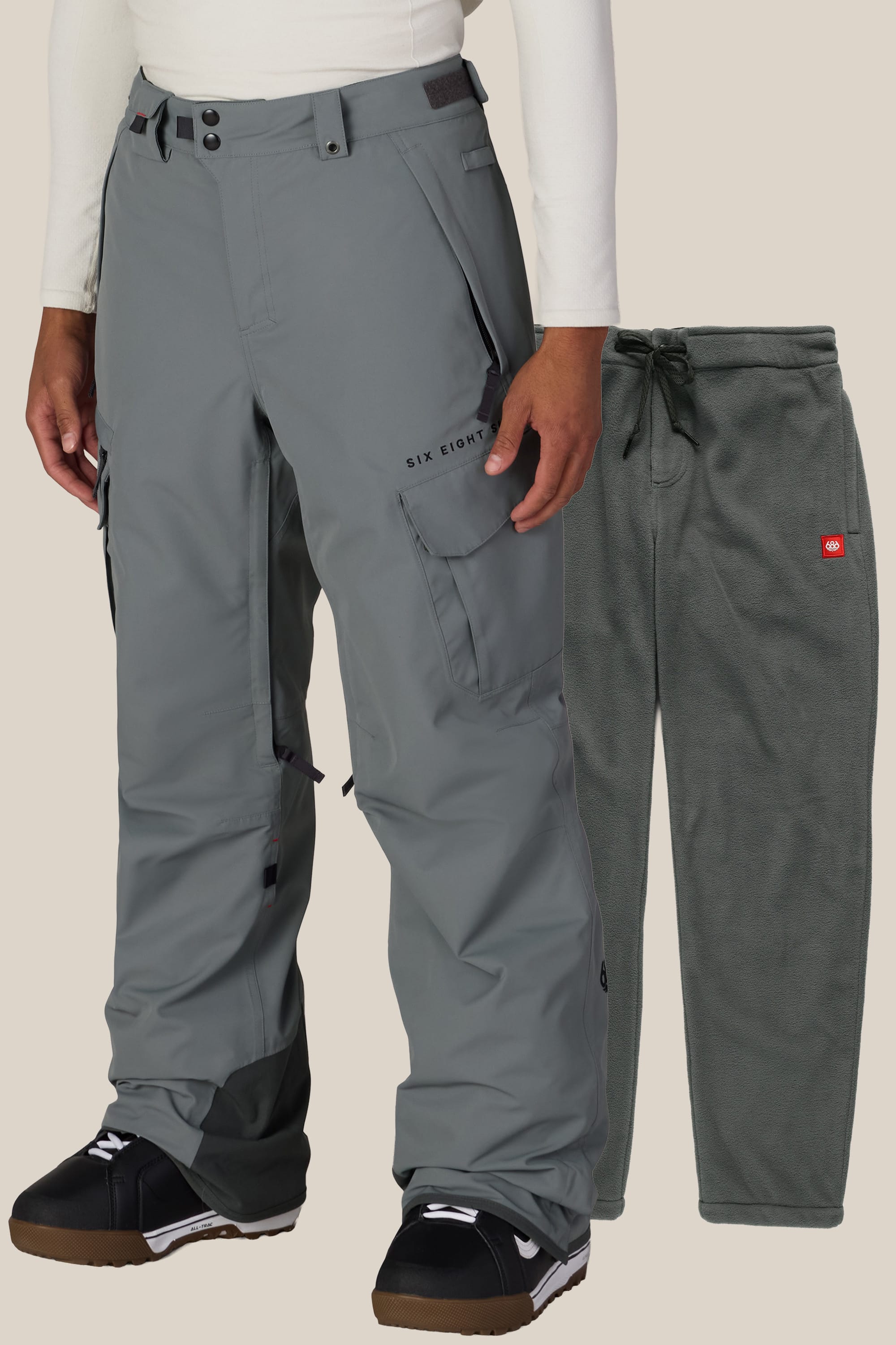 A person wears the 686 Men’s SMARTY® 3-in-1 Cargo Pant in gray with black boots. Next to them, matching gray fleece pants featuring a red logo and drawstring waist are displayed against a plain background.