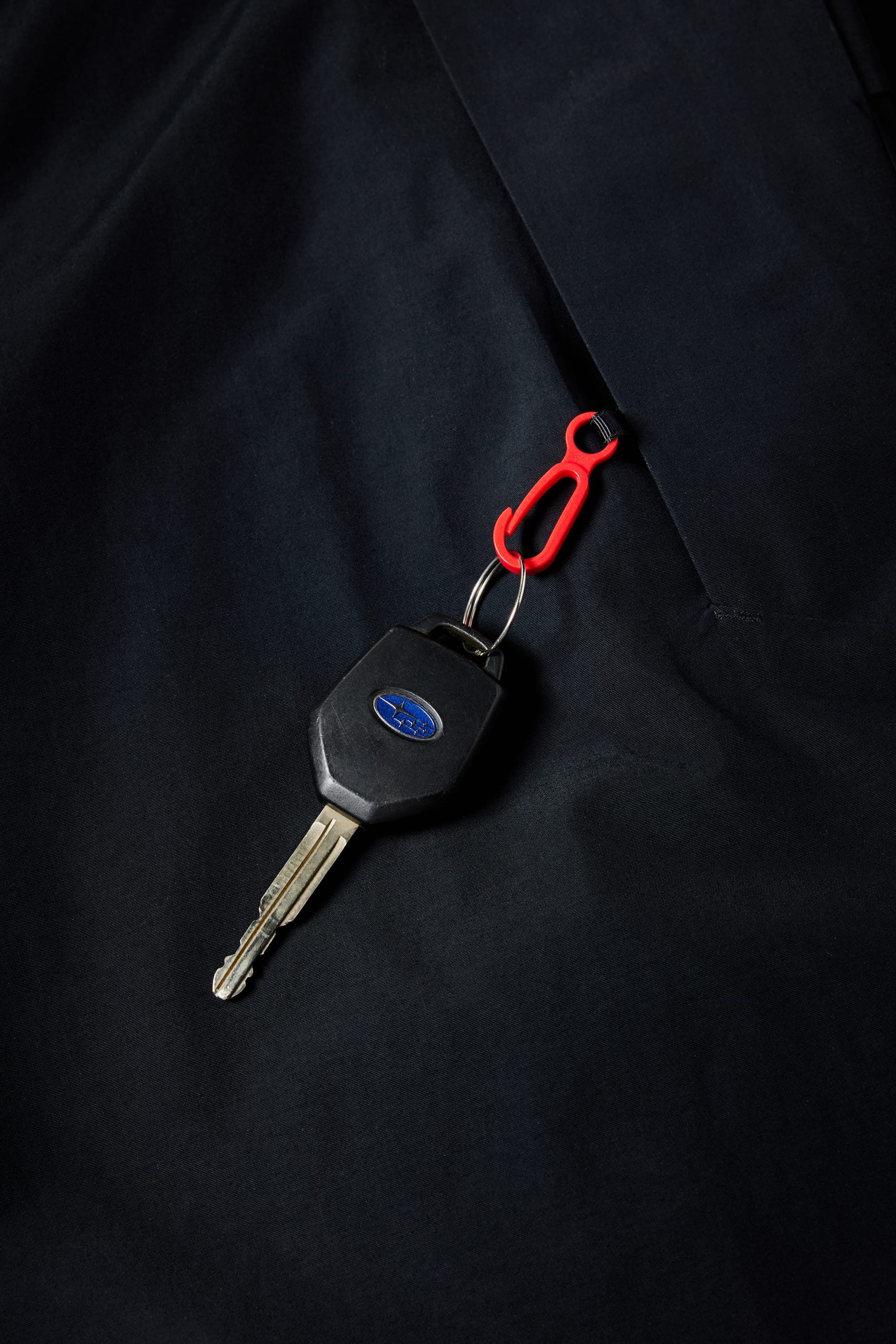 A car key with a black plastic head and silver blade is clipped to a small red carabiner, resting on dark fabric—ideal for keeping in the 686 Men's SMARTY® 3-in-1 Cargo Pant from 686, featuring a removable liner and three versatile wear options.
