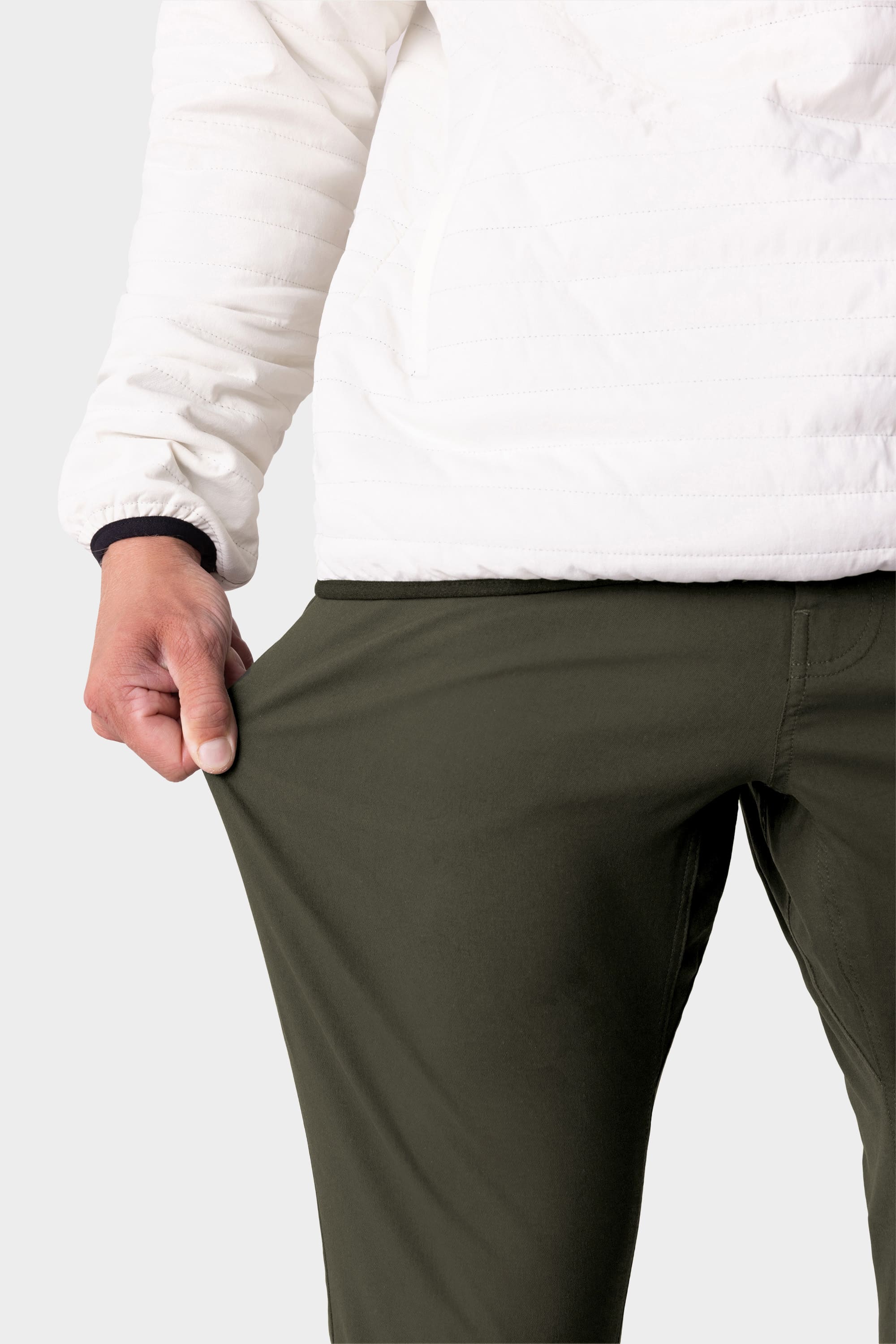 A person in an off-white jacket and 686 Men's Everywhere® Pant - Slim Fit in olive green stretches the fabric with one hand, showing the breathability and flexibility of these 686 pants.