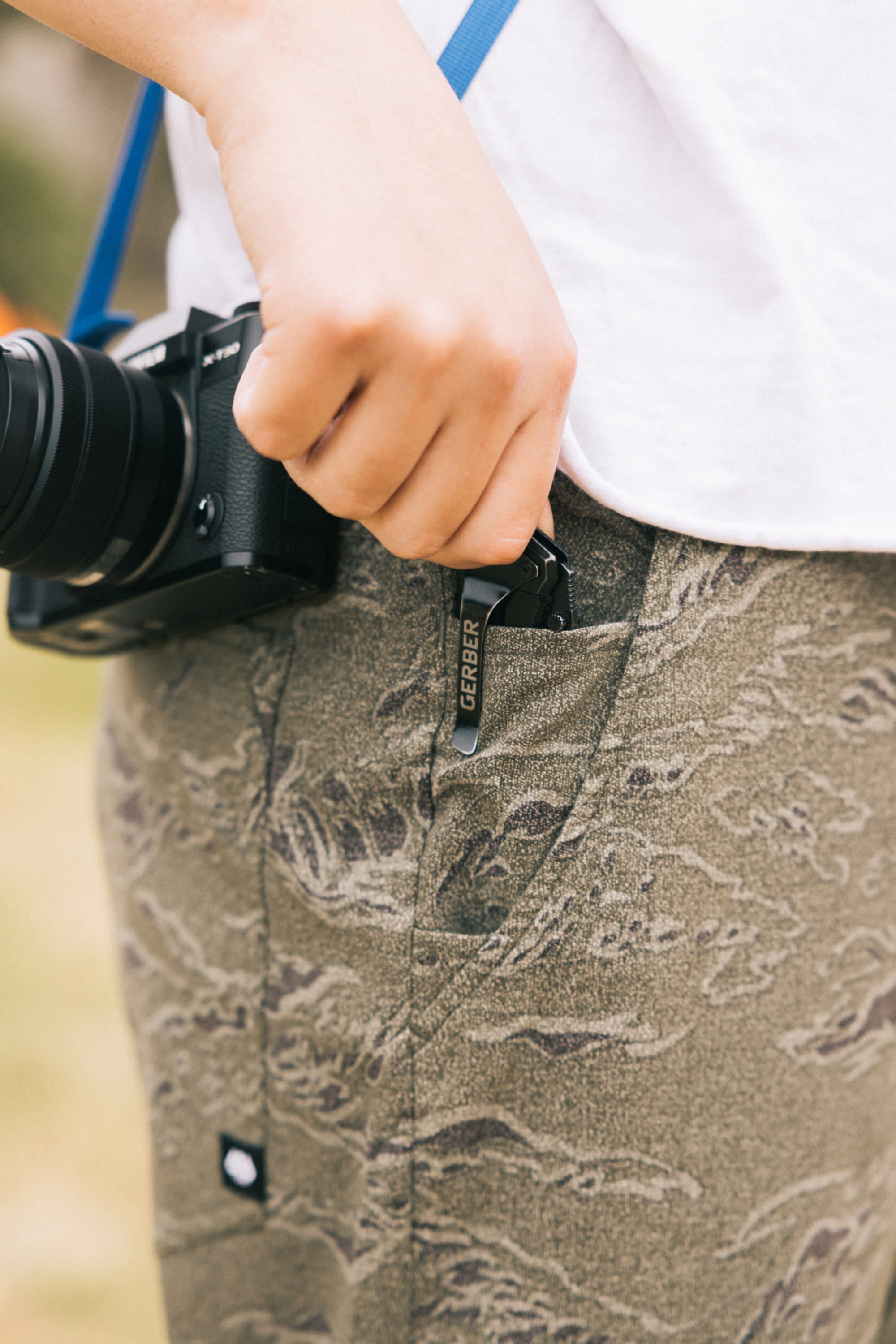Someone wearing 686 Men's Everywhere® Pant - Slim Fit has a Gerber multitool clipped to their pocket and a black camera hanging from a blue strap around their neck.