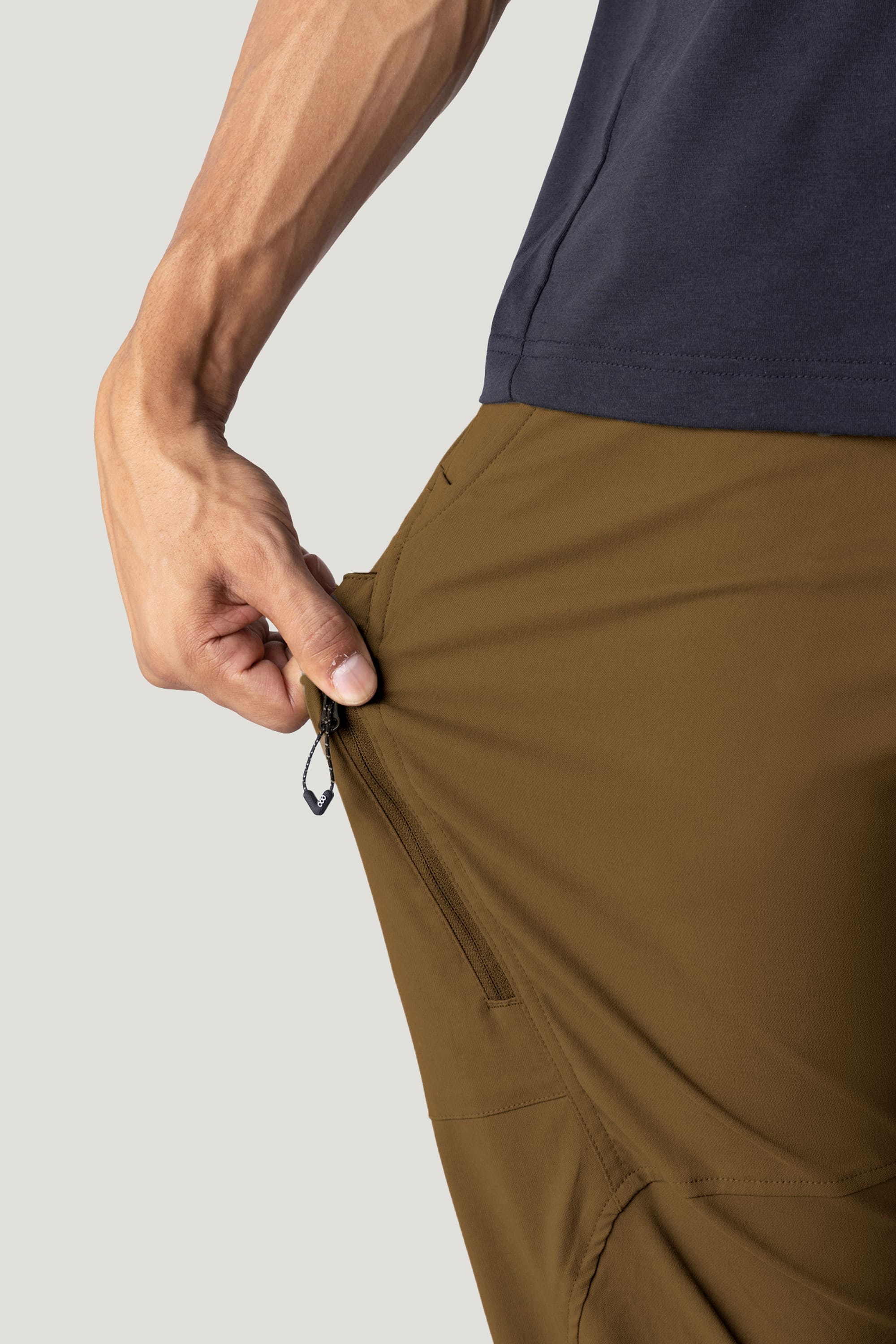 Wearing the 686 Men’s Anything Cargo Pant - Relaxed Fit in brown, a person pulls on the side zipper pocket, demonstrating the pant's impressive 4-way stretch and flexibility.