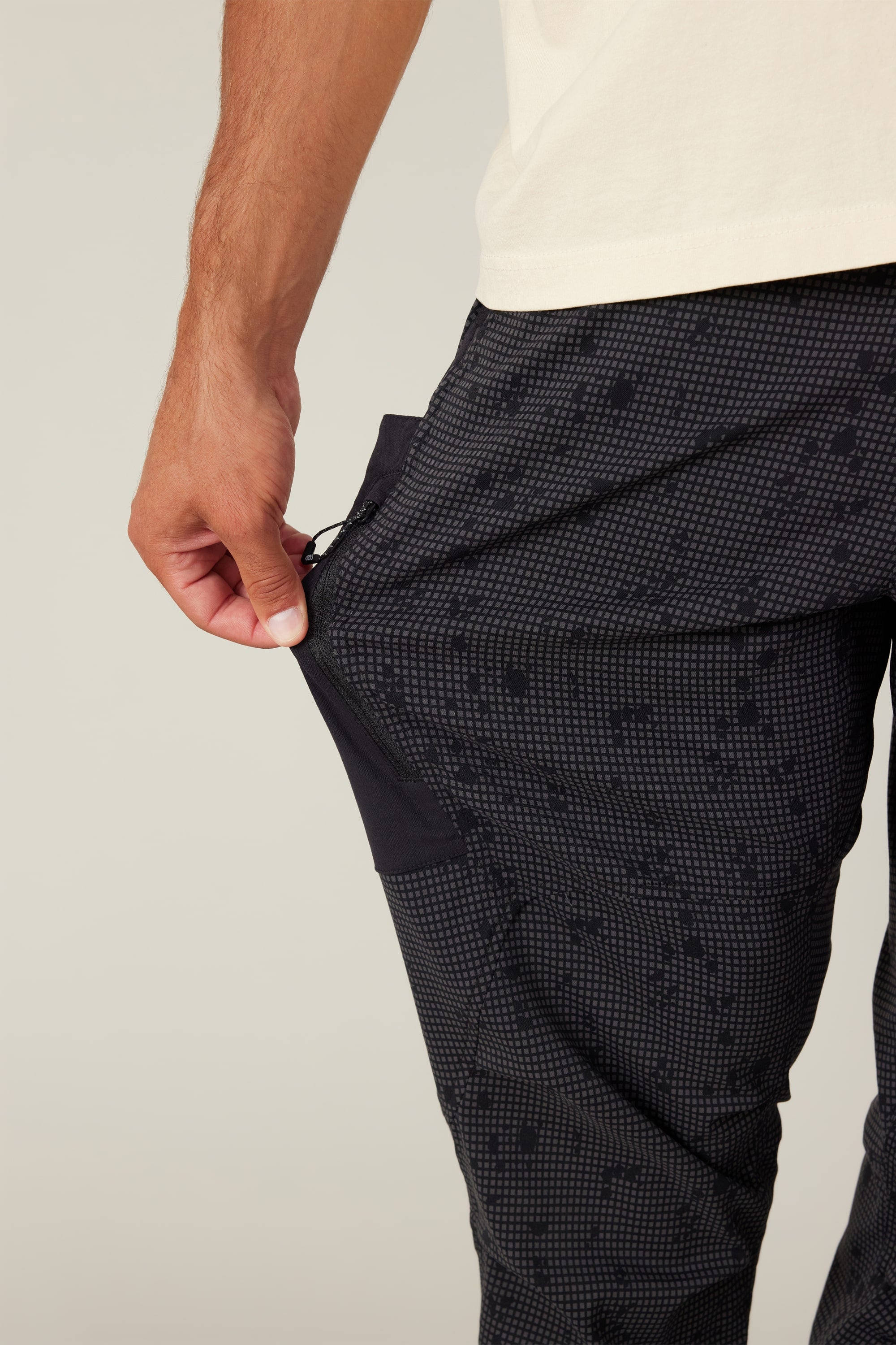 A person wearing 686 Men's Anything Cargo Pant - Slim Fit is unzipping a side pocket on their thigh with one hand; only their lower torso and hand are visible.