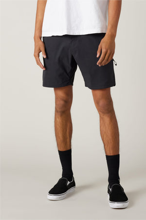 A person wearing a white T-shirt, 686 Men's Everywhere¨ Featherlight Chino Short in black, black socks, and black slip-on shoes stands against a plain light background; only the body from shoulders down is visible.