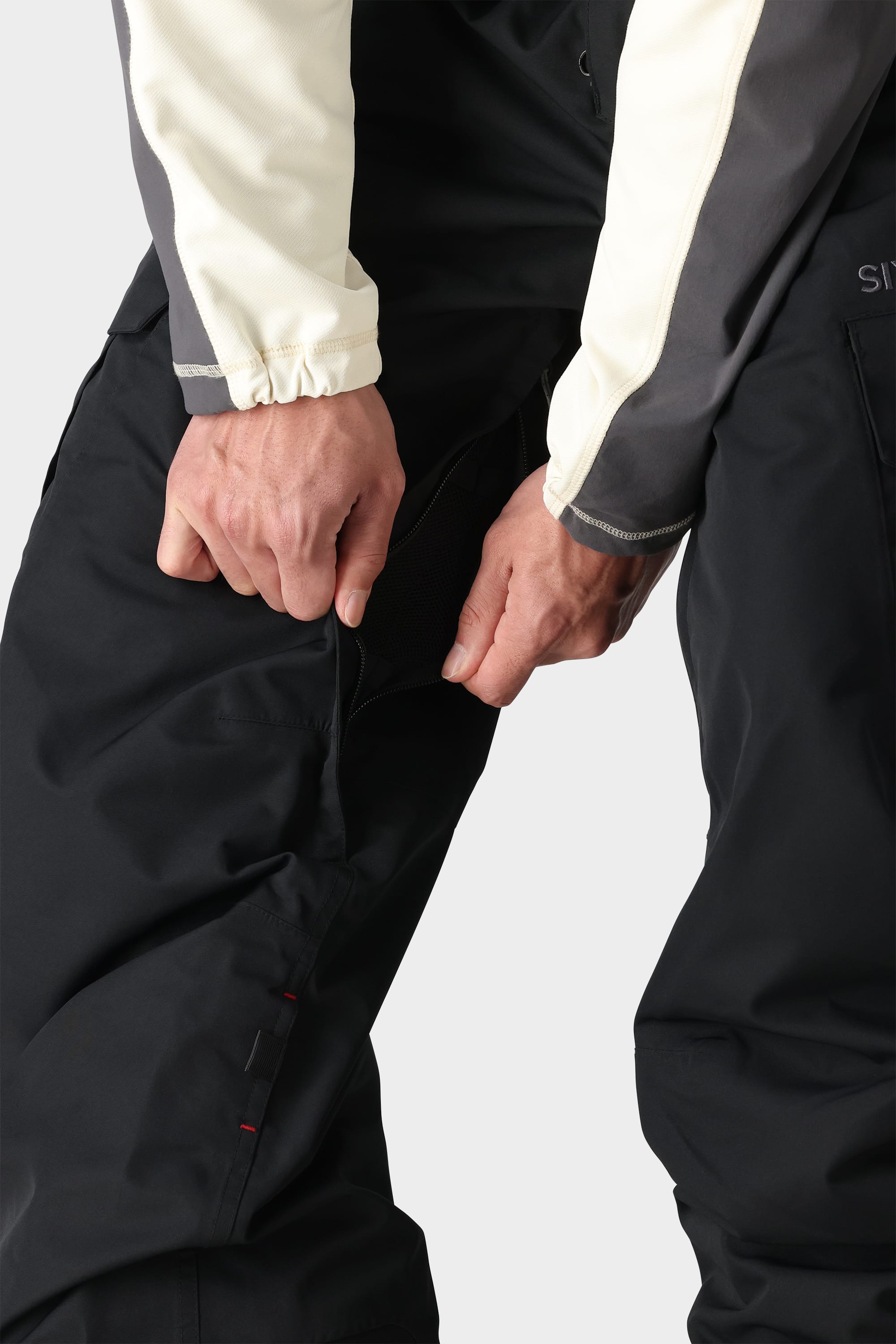 A person wearing the 686 Men's SMARTY® 3-in-1 Cargo Bib unzips a ventilation zipper on the thigh area of the shell bib.
