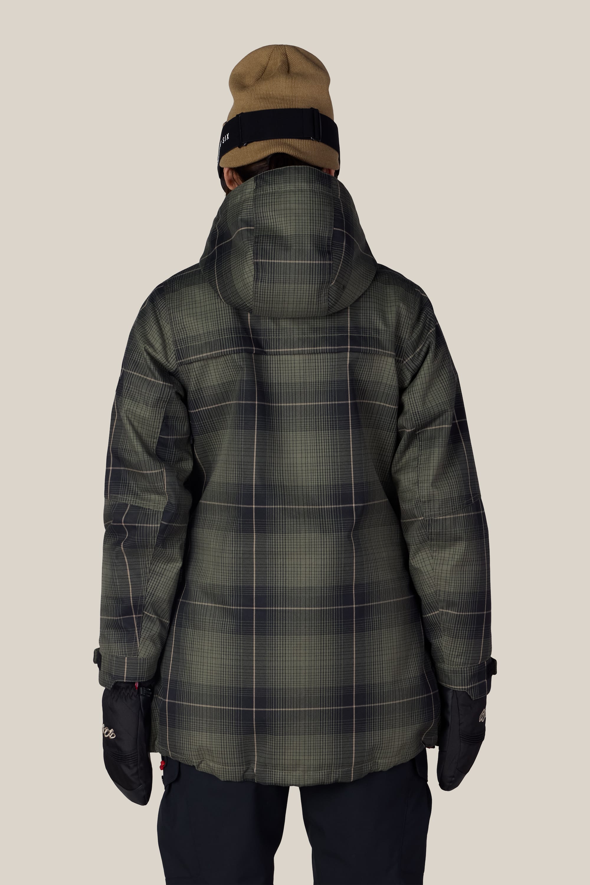 A person wearing the 686 Women’s Spirit Insulated Jacket by 686, along with black gloves and a tan beanie, is facing away from the camera against a plain light background.