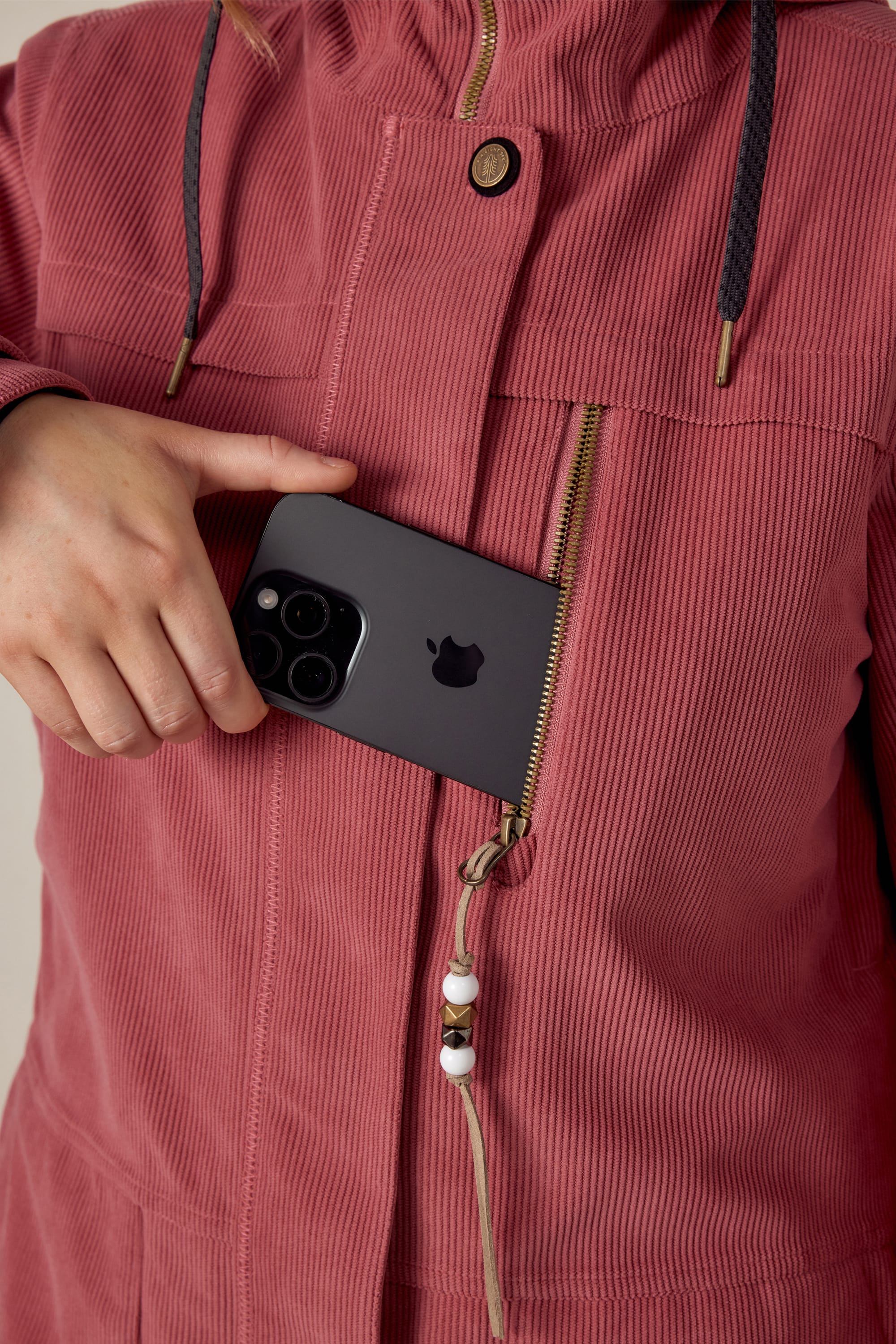 A woman wearing the 686 Womens Spirit Insulated Jacket places a black smartphone with three camera lenses into the zippered chest pocket of her pink, faux-fur lined jacket by 686.