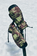 Two patterned 686 Lander™ Mitts with light insulation and waterproofing, featuring the 686 logo, are placed atop crossed ski poles against a snowy backdrop.
